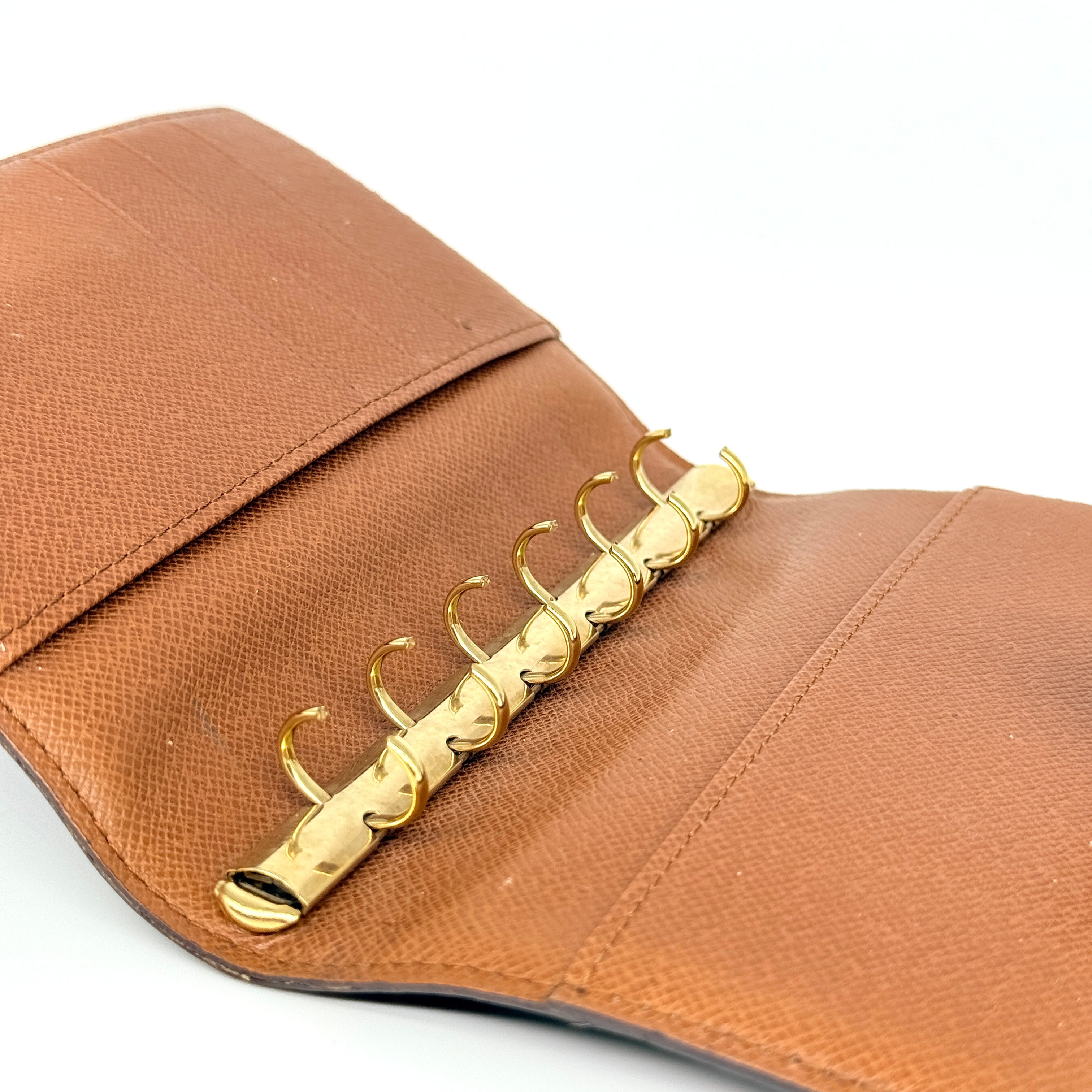 Louis Vuitton Monogram Agenda Cover in brown canvas with gold snap closure, displayed against a white background.