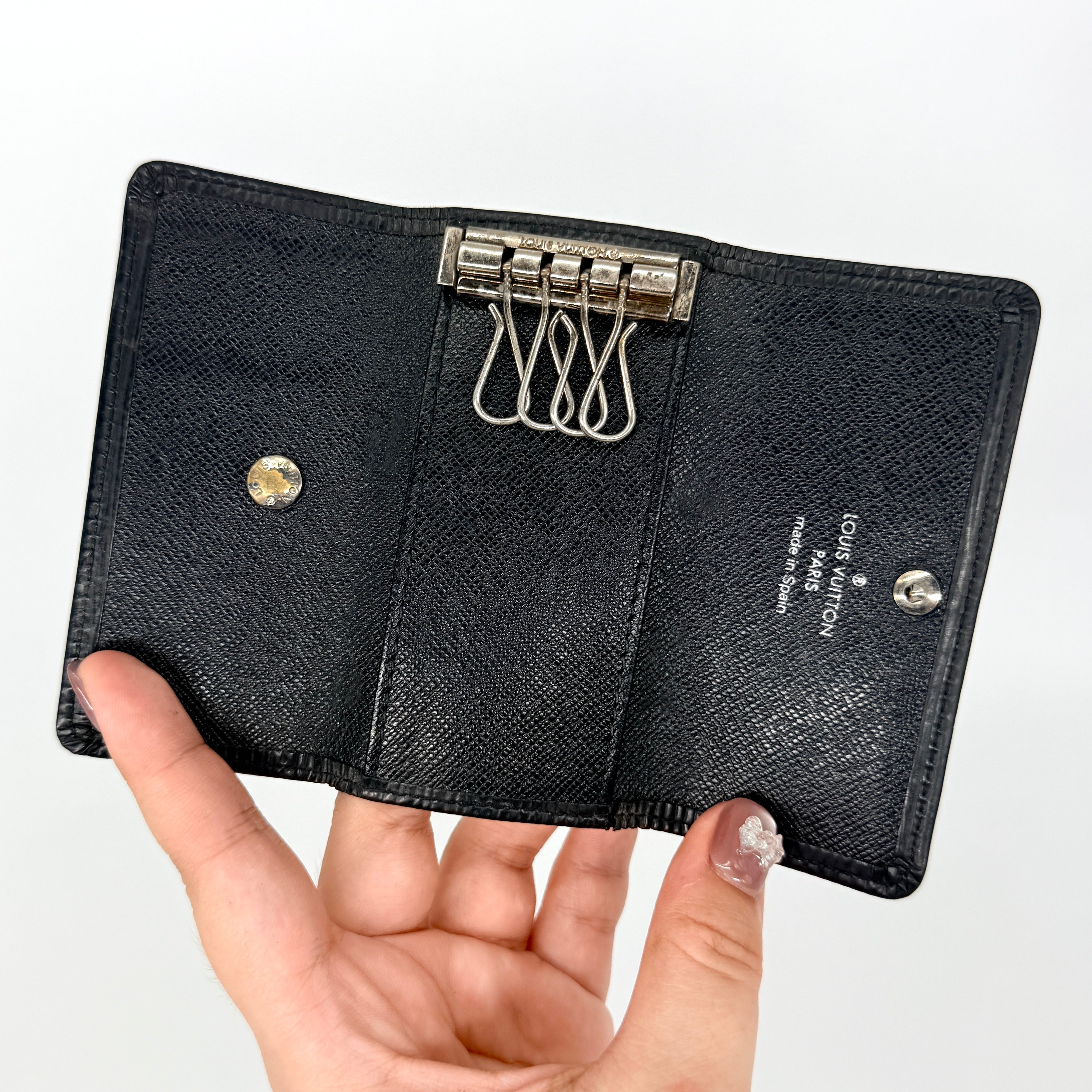 Louis Vuitton Epi Leather key case in black with silver-tone key hooks and snap closure, photographed against a clean white background.