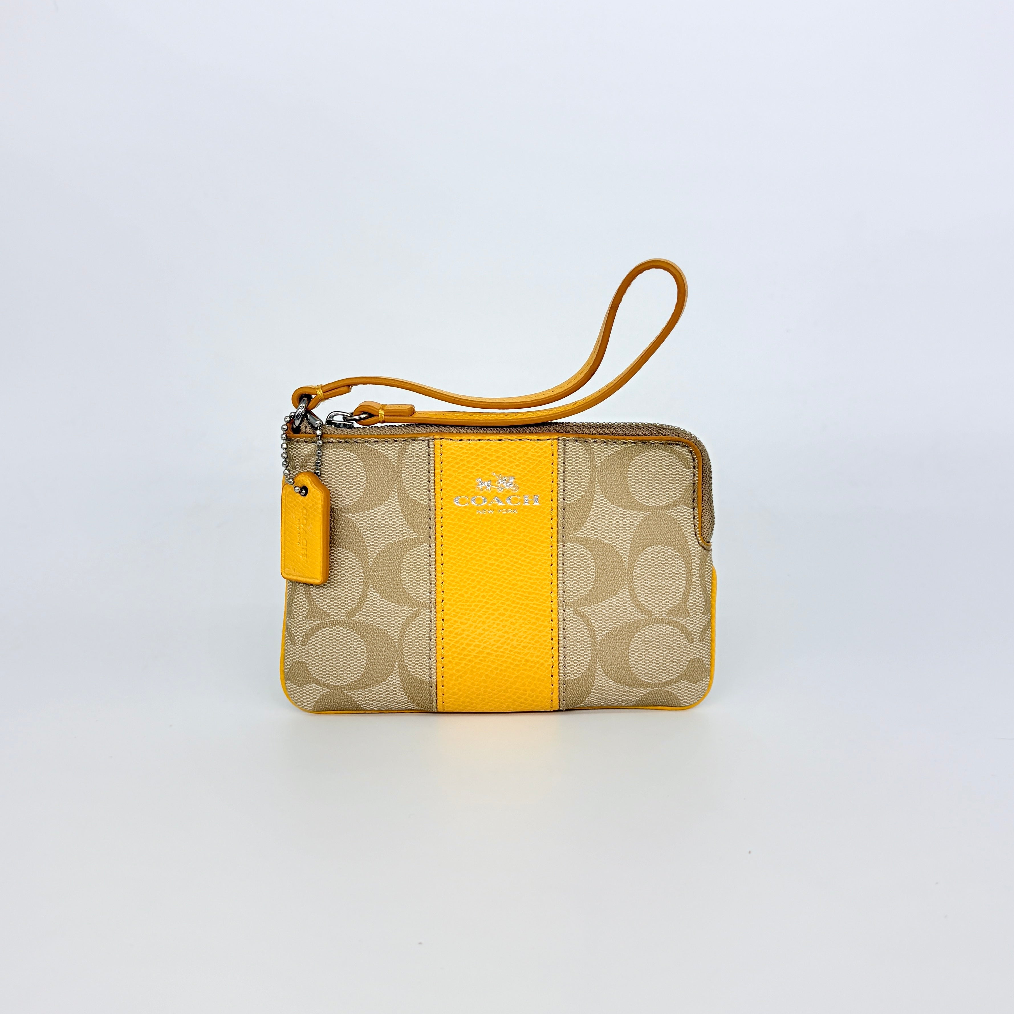 Coach Signature Stripe Corner Zip Wristlet in beige canvas with bold yellow leather stripe, silver hardware, and wrist strap displayed on a white background.