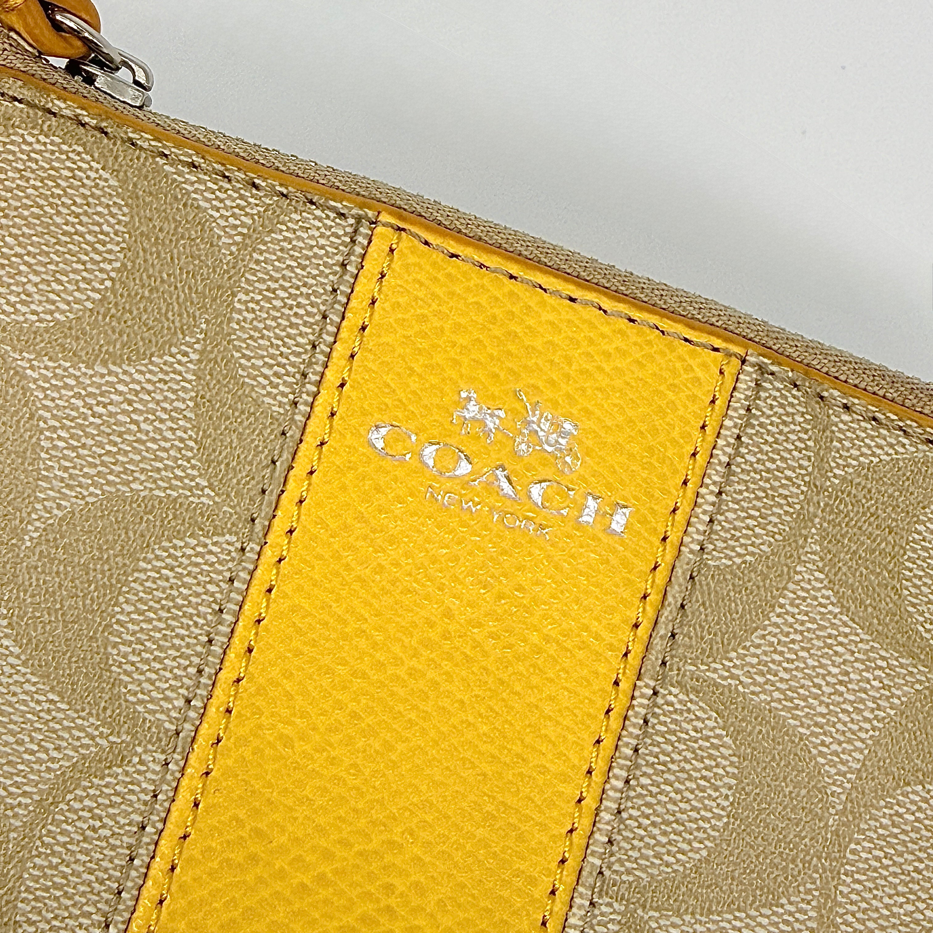 Coach Signature Stripe Corner Zip Wristlet in beige canvas with bold yellow leather stripe, silver hardware, and wrist strap displayed on a white background.