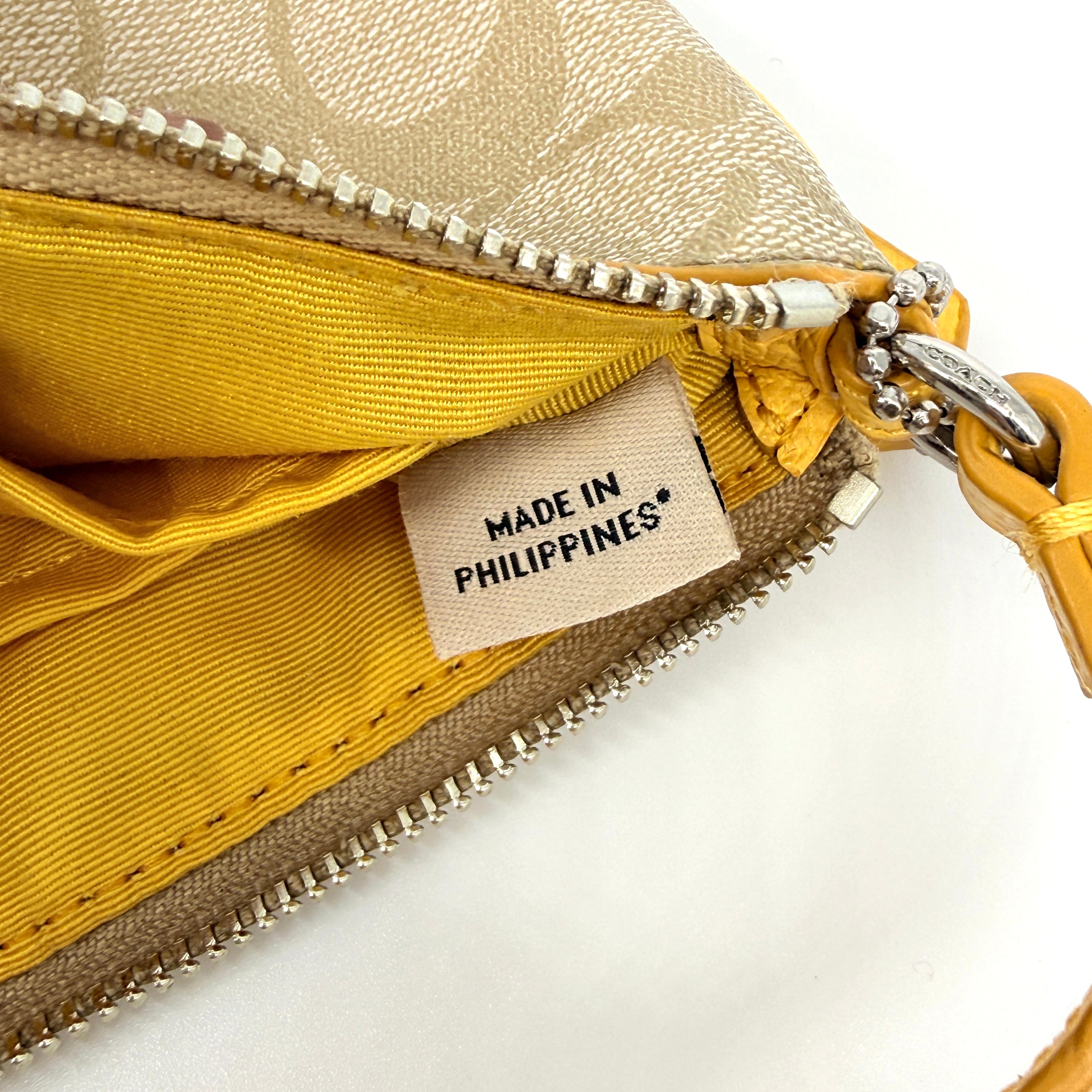 Coach Signature Stripe Corner Zip Wristlet in beige canvas with bold yellow leather stripe, silver hardware, and wrist strap displayed on a white background.