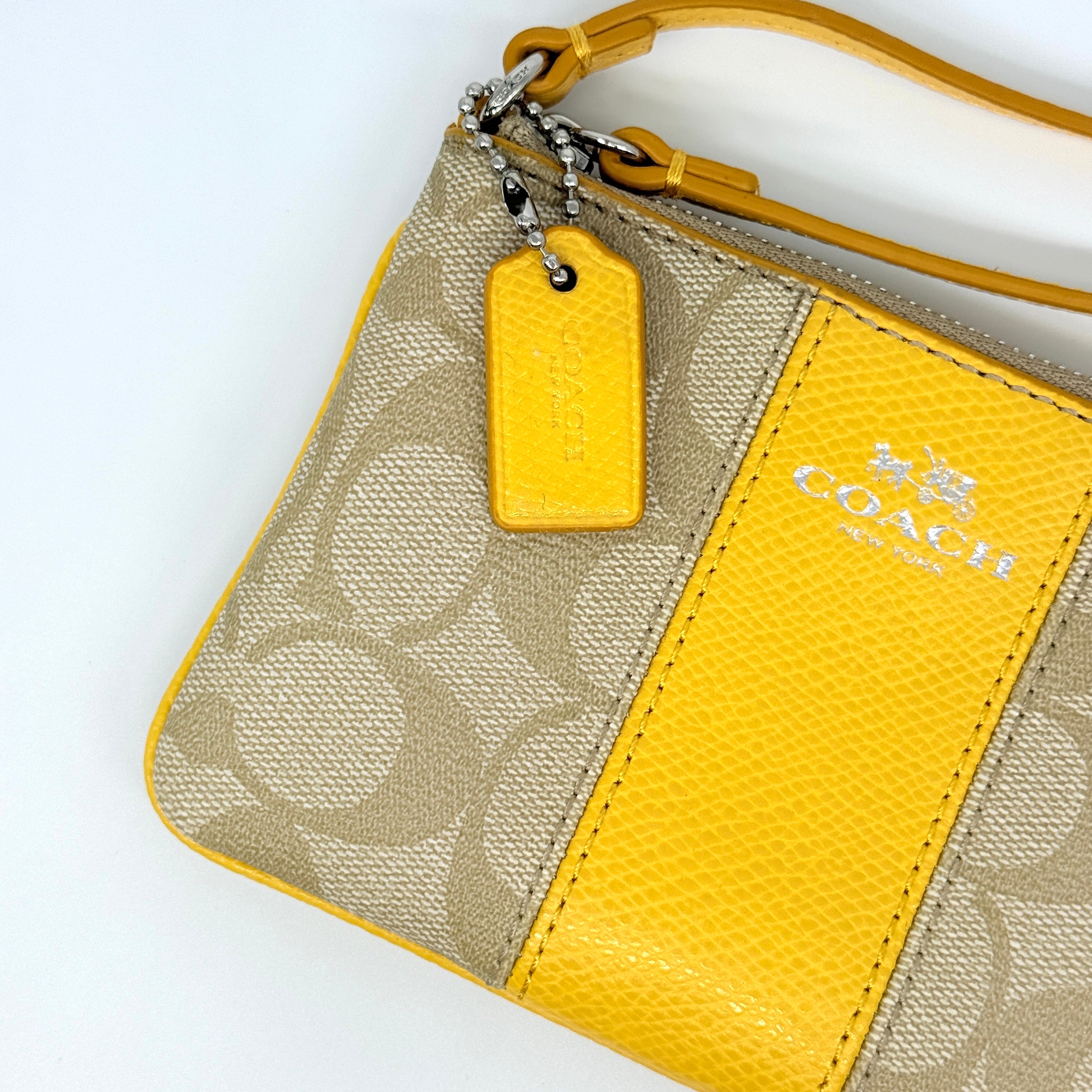 Coach Signature Stripe Corner Zip Wristlet in beige canvas with bold yellow leather stripe, silver hardware, and wrist strap displayed on a white background.