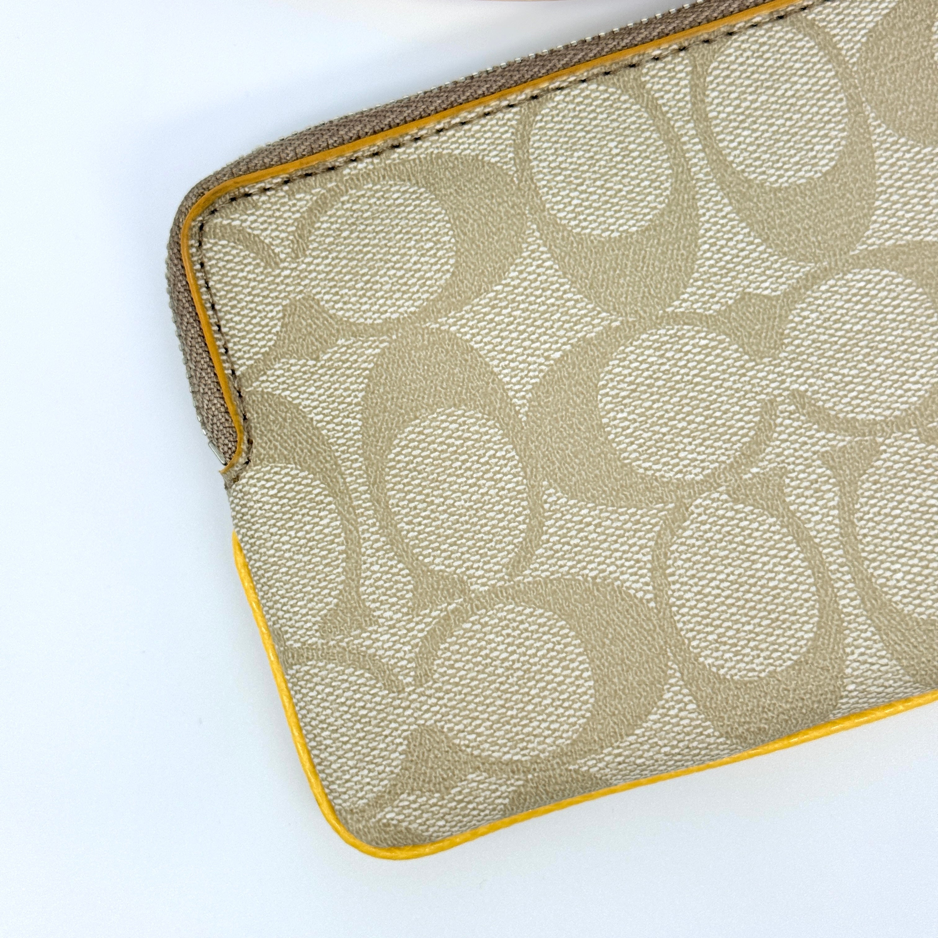 Coach Signature Stripe Corner Zip Wristlet in beige canvas with bold yellow leather stripe, silver hardware, and wrist strap displayed on a white background.