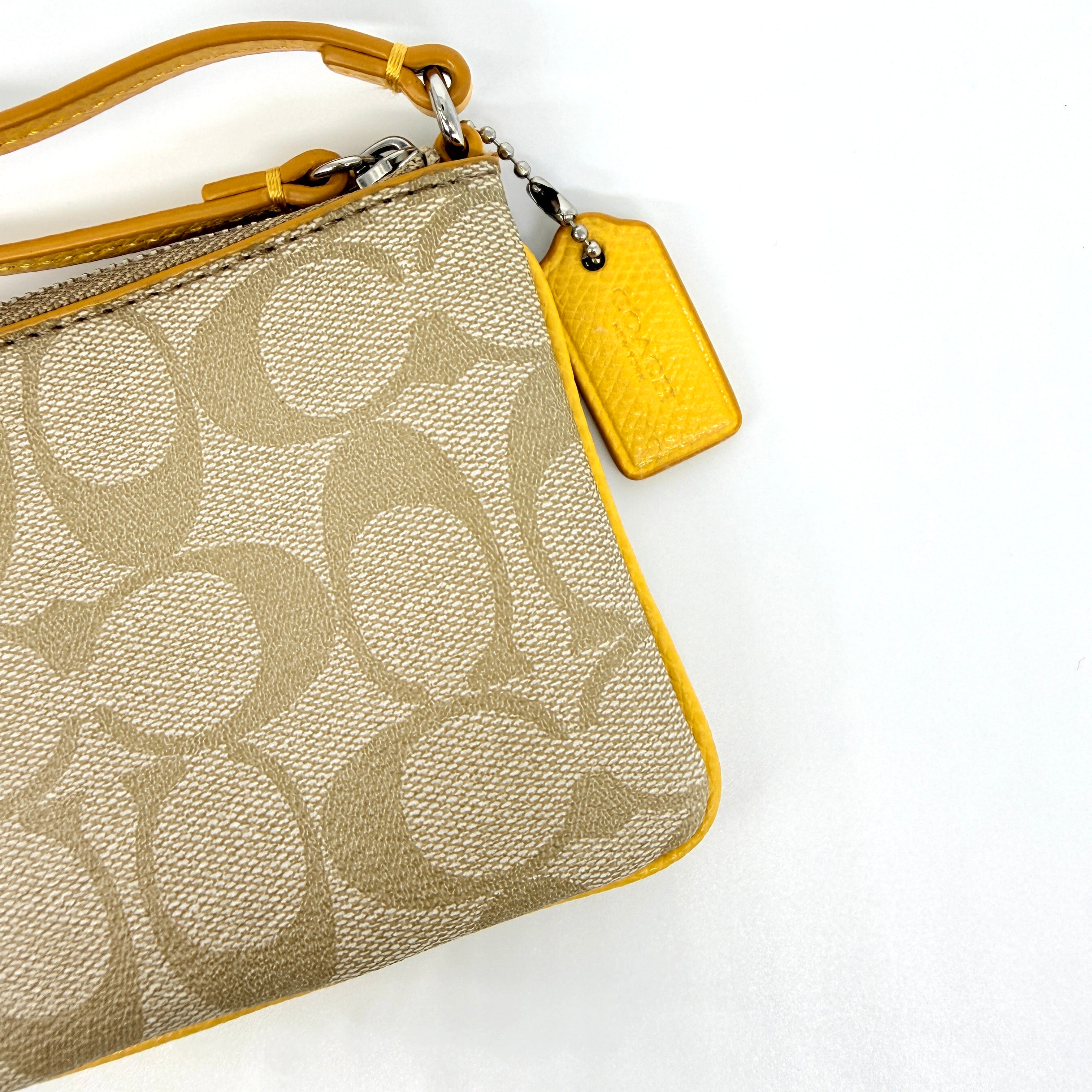 Coach Signature Stripe Corner Zip Wristlet in beige canvas with bold yellow leather stripe, silver hardware, and wrist strap displayed on a white background.
