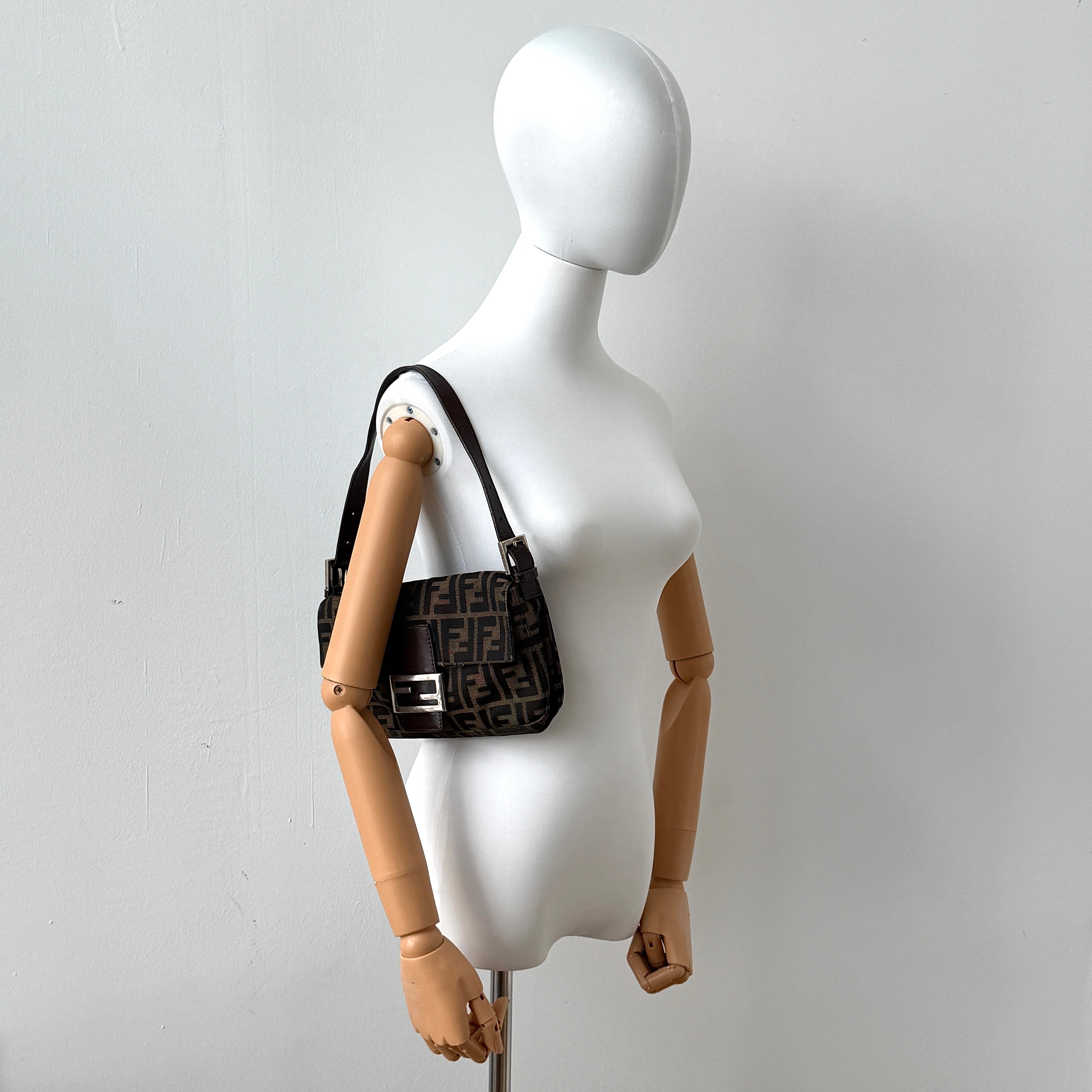 Fendi Zucca Print Baguette Bag in brown monogram canvas with silver-tone FF clasp and leather trim shown against a white background.