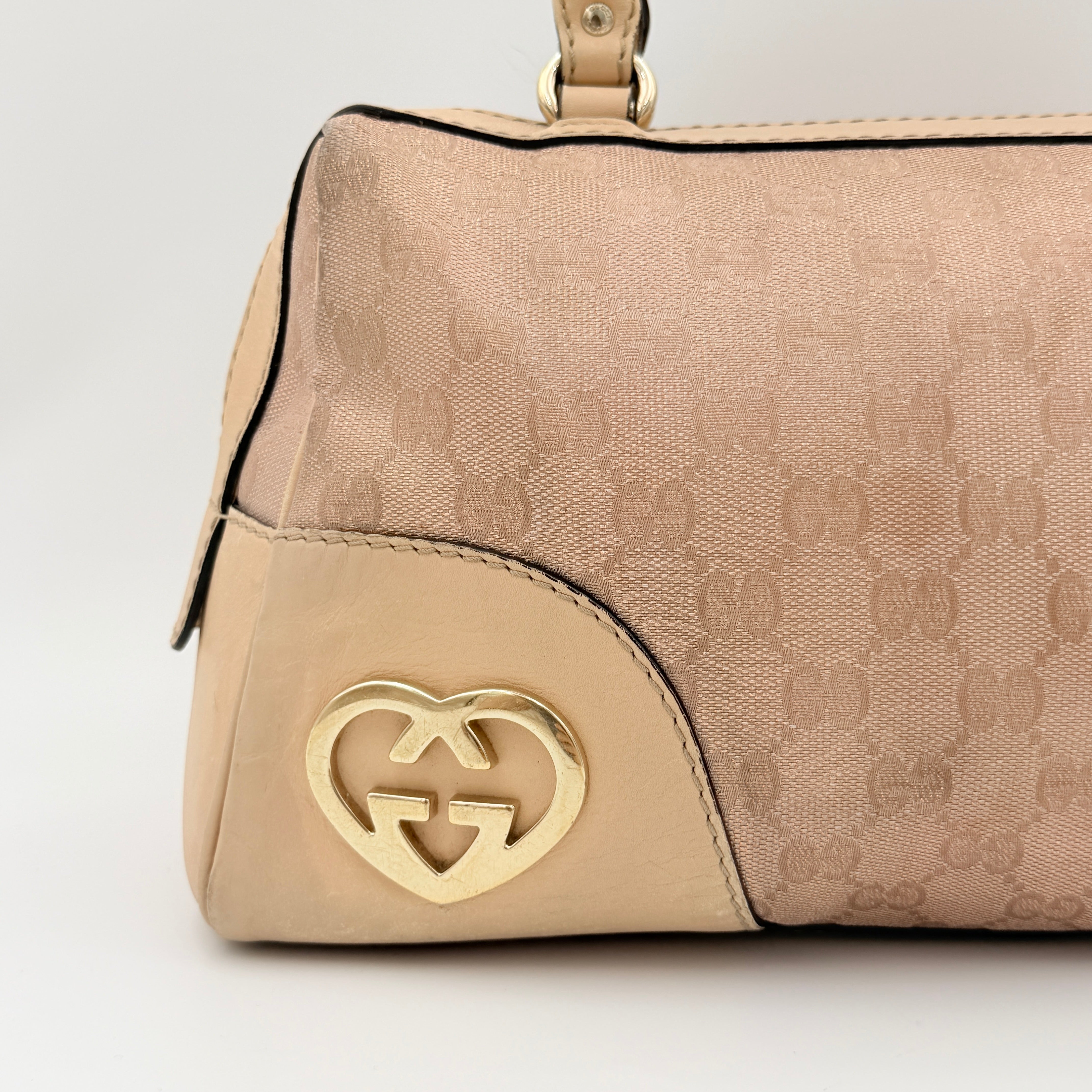 Gucci GG Monogram Heart Lovely Boston Bag in beige and pink with gold heart logo and double handles, displayed against a plain background.
