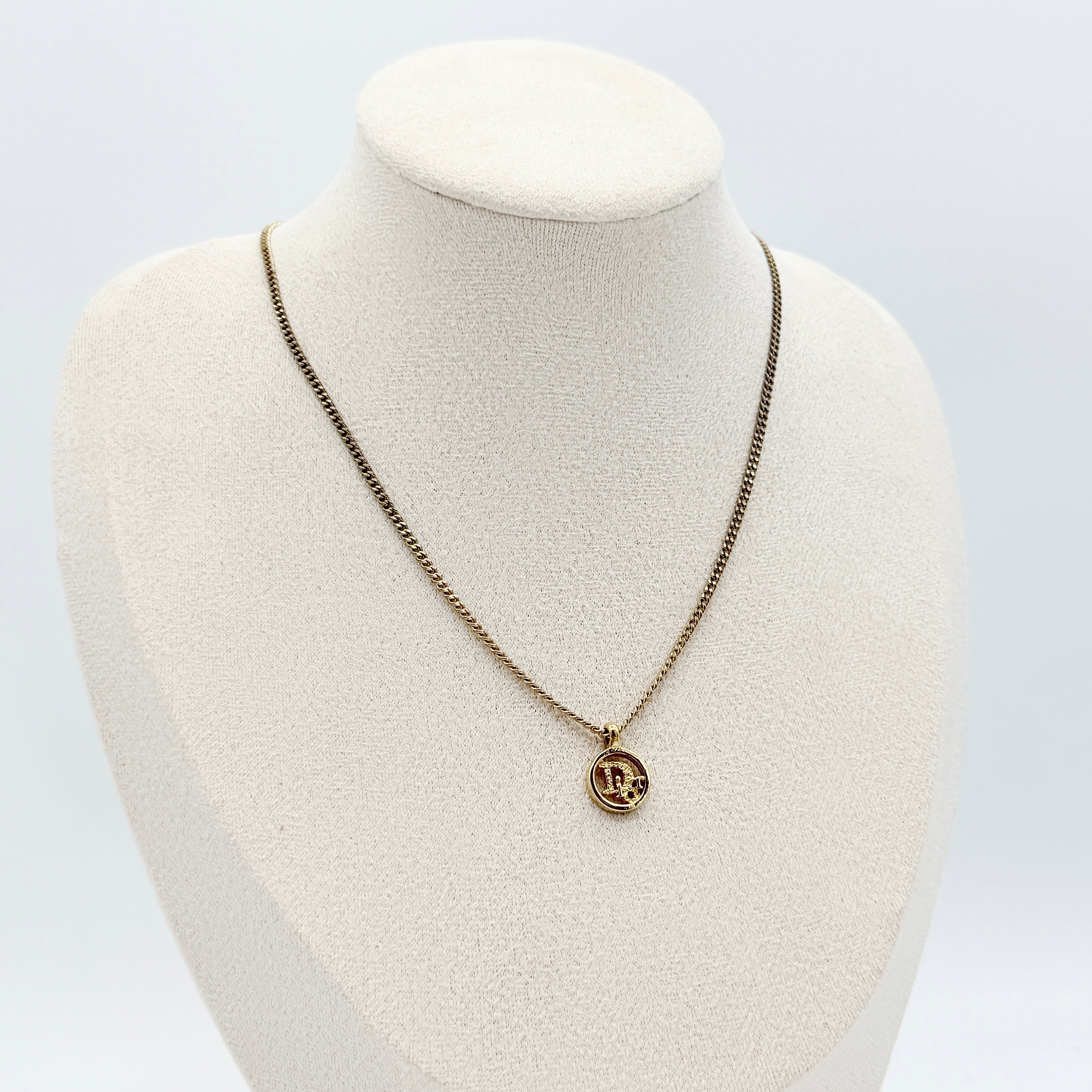 Dior gold-tone necklace featuring a circular logo pendant displayed on a necklace stand.