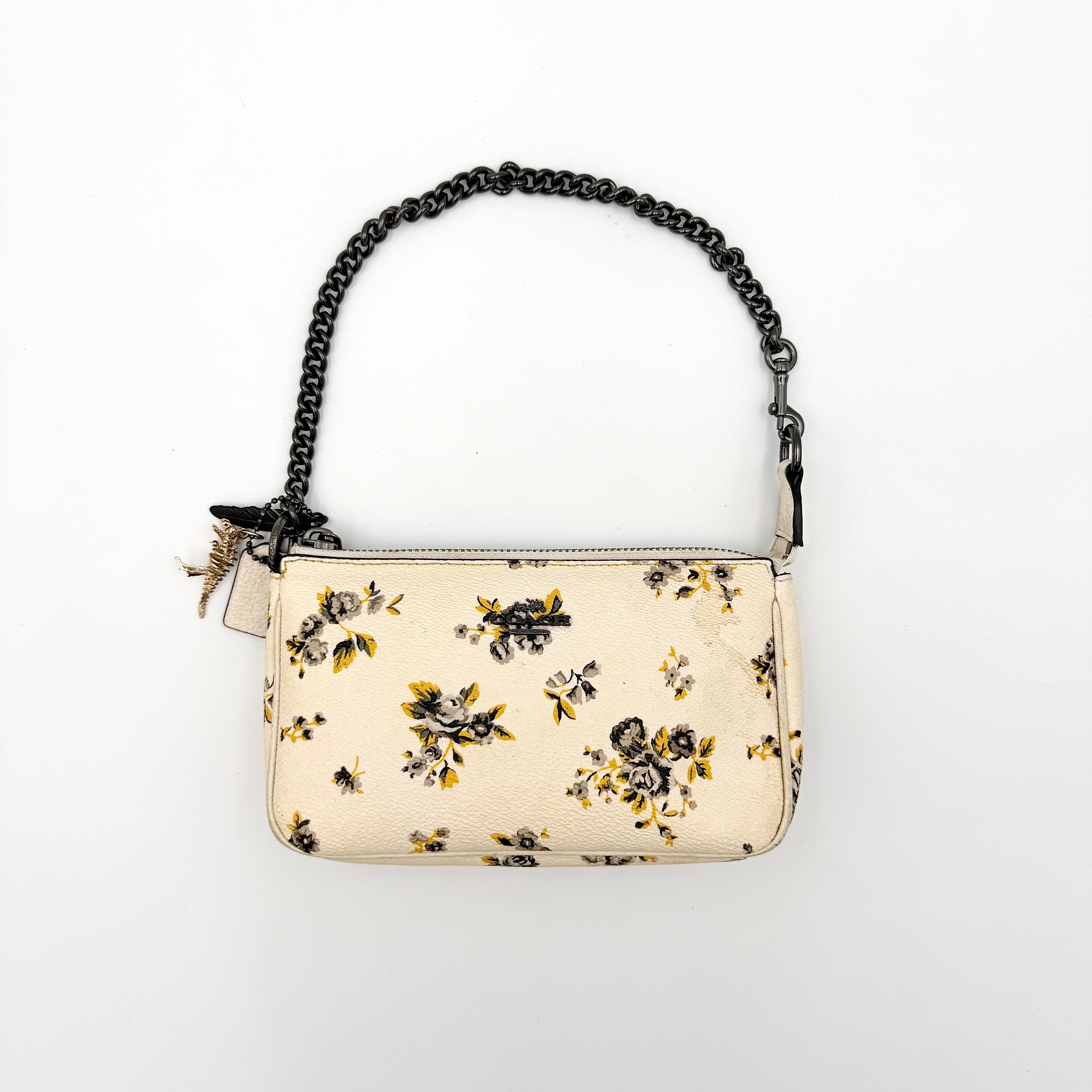 Coach Nolita 19 shoulder bag in white pebbled leather with yellow and grey floral print, chunky gunmetal chain strap, and decorative charms.