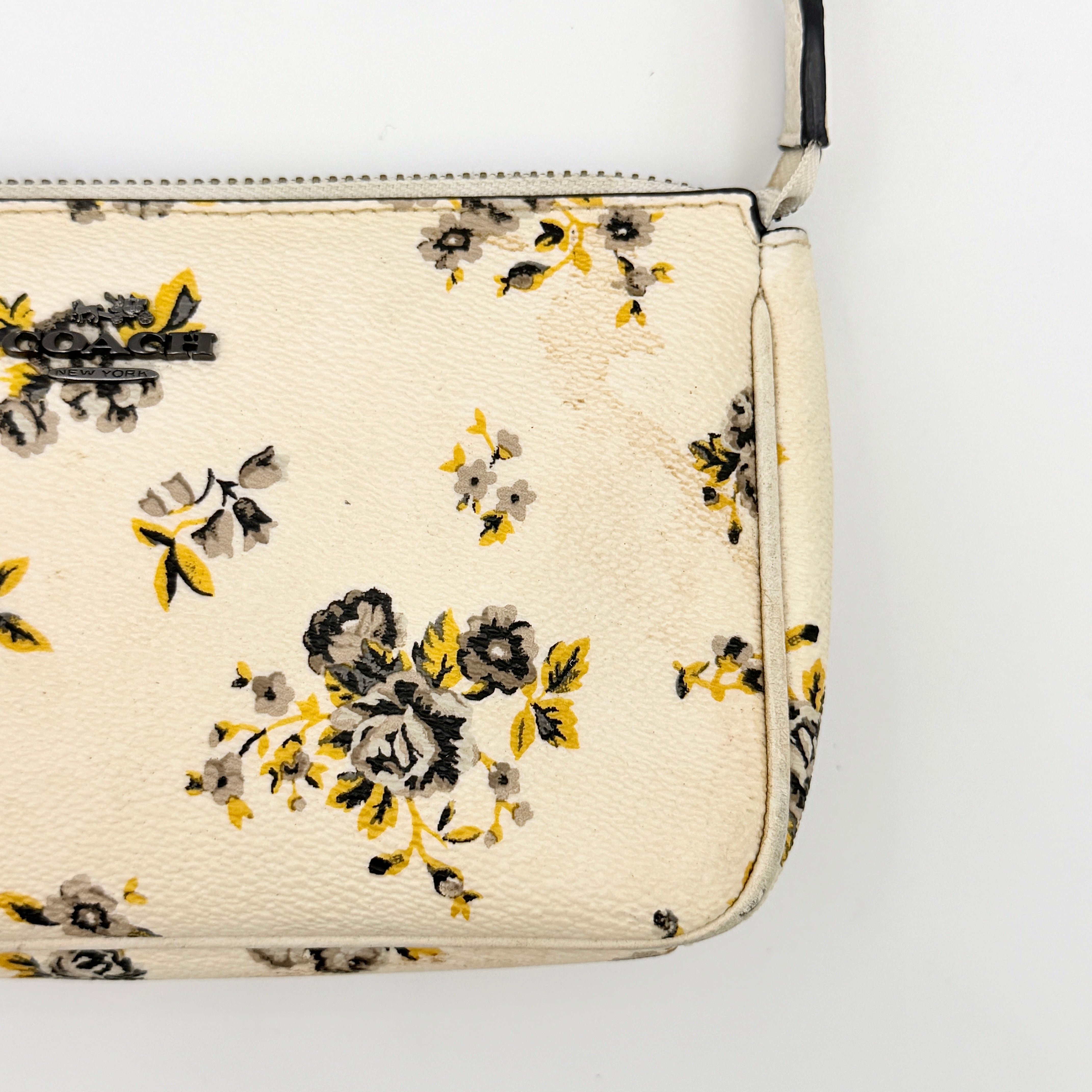 Coach Nolita 19 shoulder bag in white pebbled leather with yellow and grey floral print, chunky gunmetal chain strap, and decorative charms.