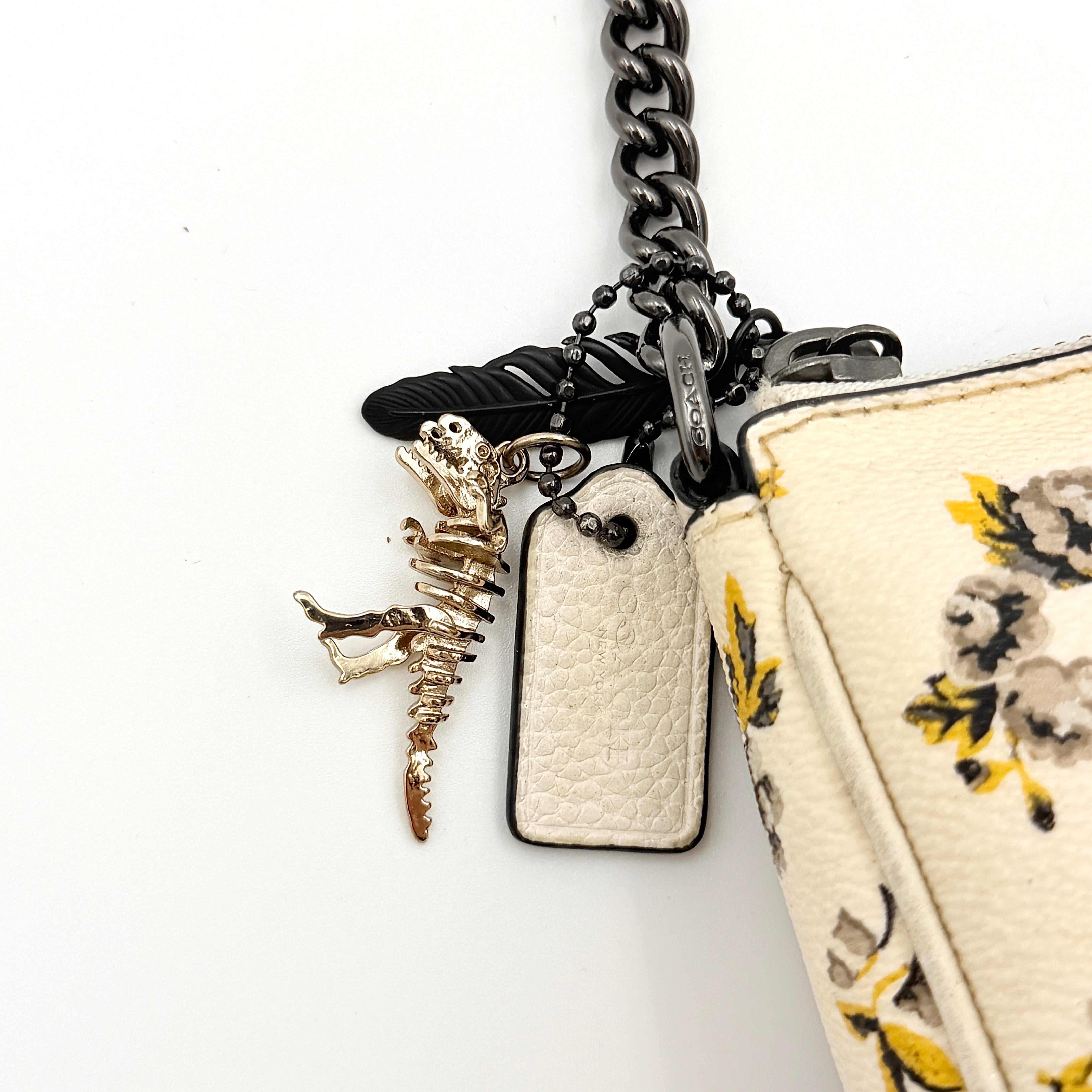 Coach Nolita 19 shoulder bag in white pebbled leather with yellow and grey floral print, chunky gunmetal chain strap, and decorative charms.