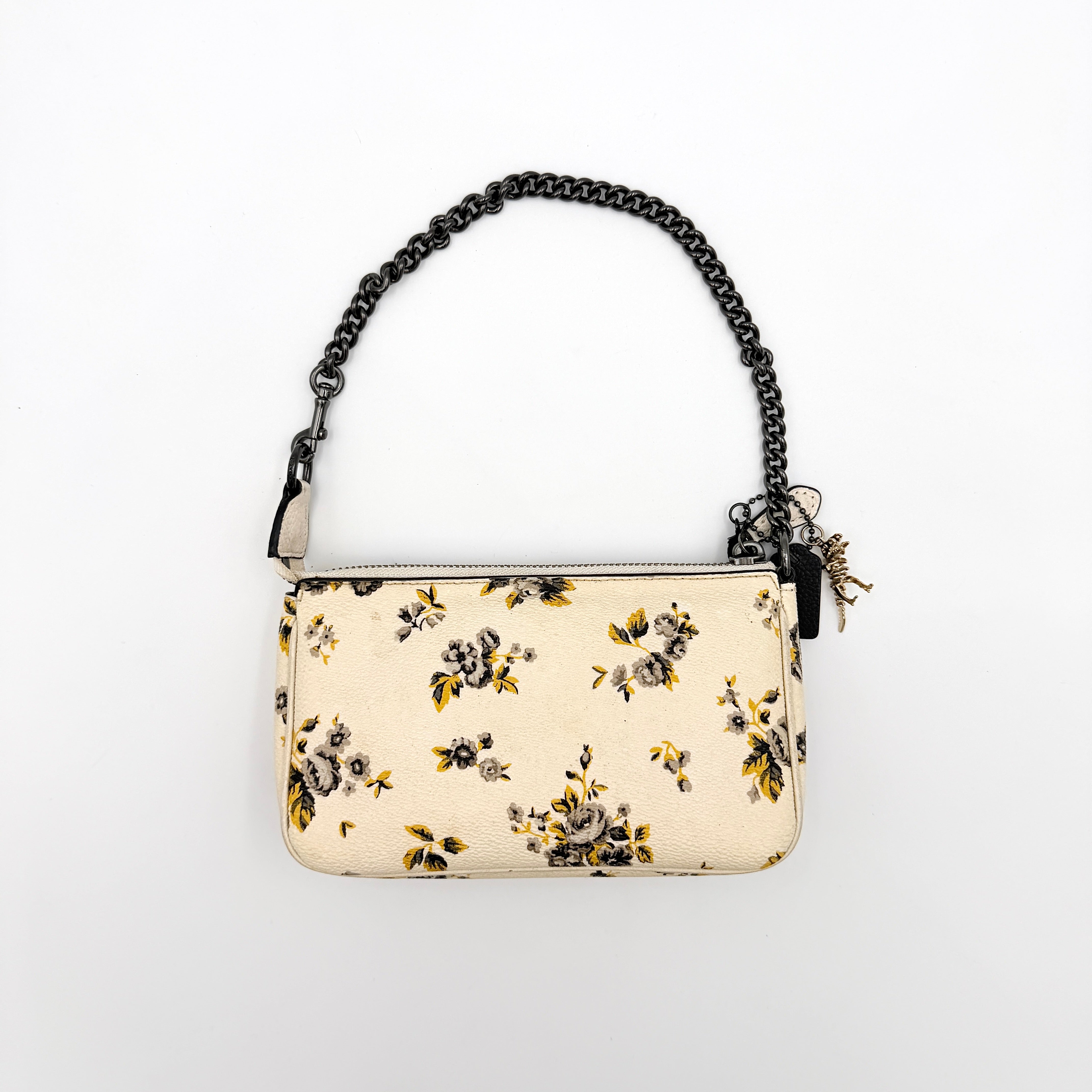 Coach Nolita 19 shoulder bag in white pebbled leather with yellow and grey floral print, chunky gunmetal chain strap, and decorative charms.