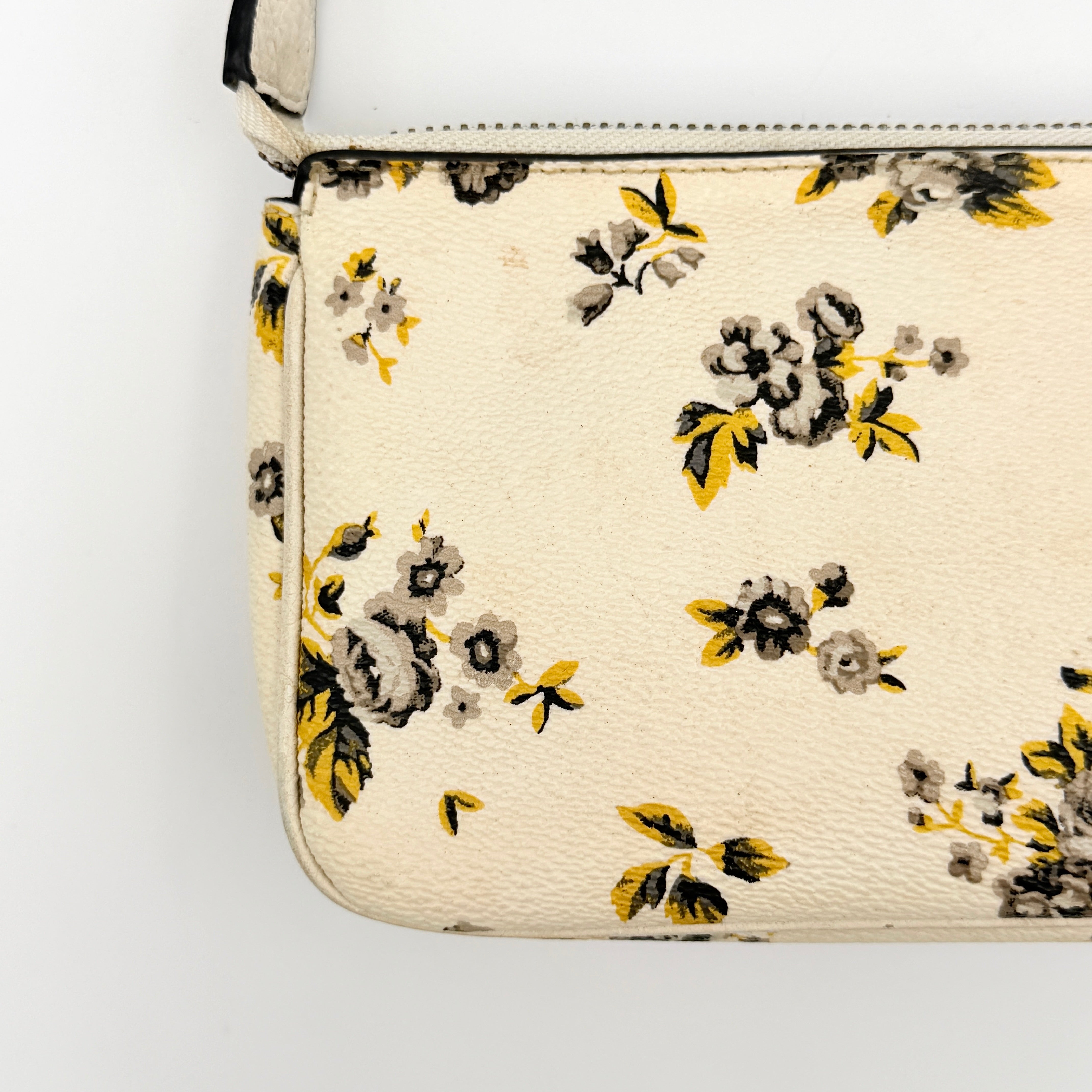 Coach Nolita 19 shoulder bag in white pebbled leather with yellow and grey floral print, chunky gunmetal chain strap, and decorative charms.
