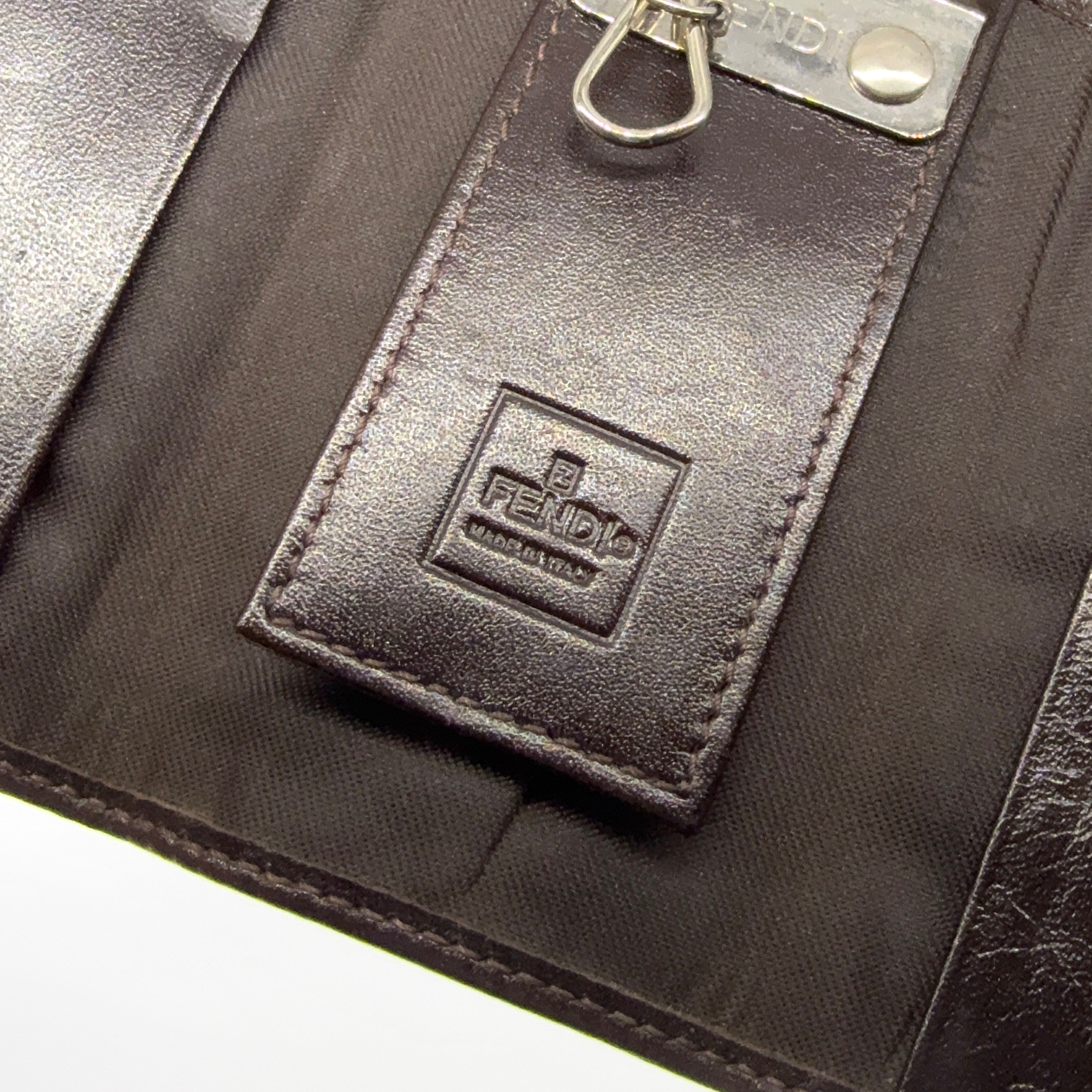 Fendi FF Zucca key case in brown canvas with dark brown leather trim and silver-tone hardware displayed closed against a white backdrop.