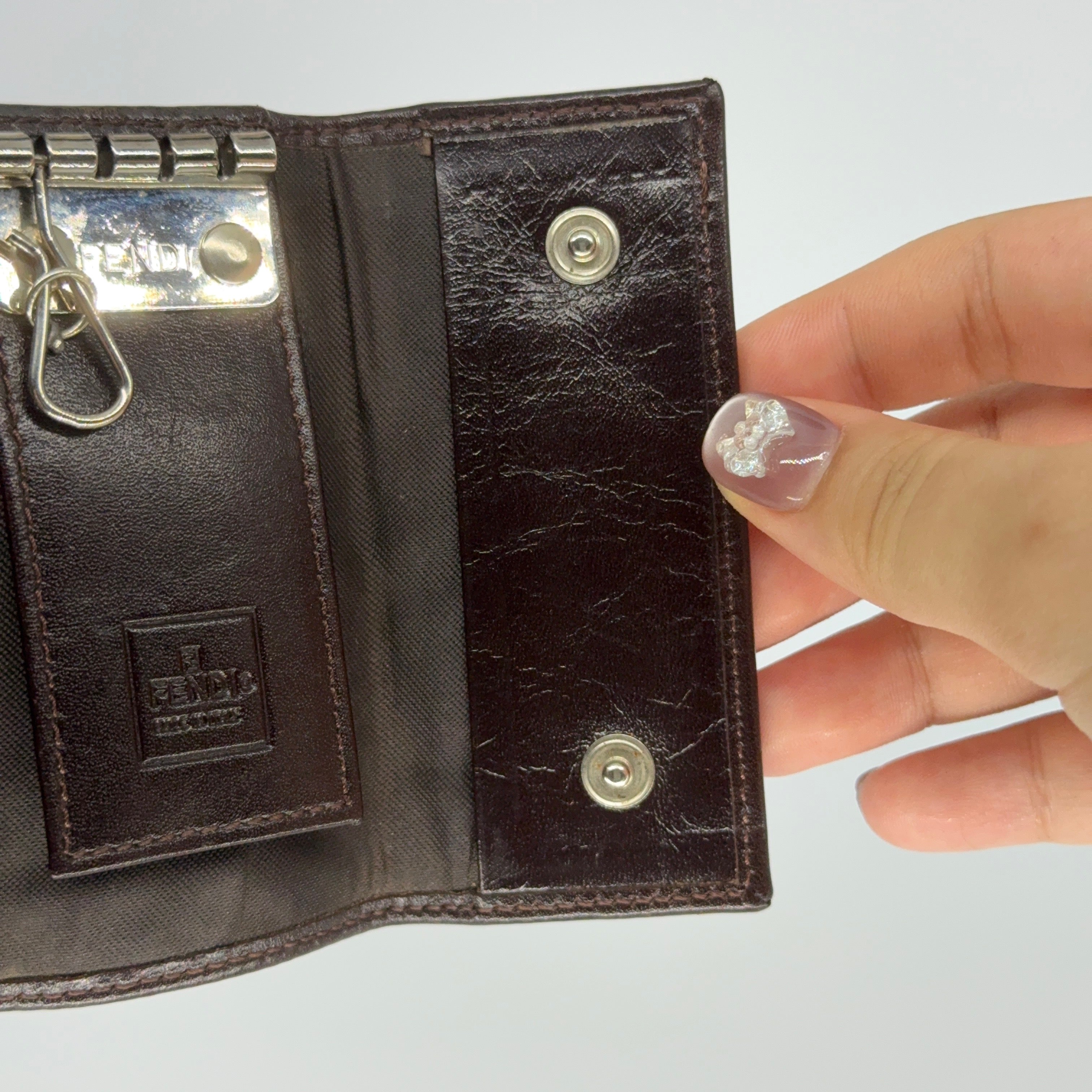 Fendi FF Zucca key case in brown canvas with dark brown leather trim and silver-tone hardware displayed closed against a white backdrop.