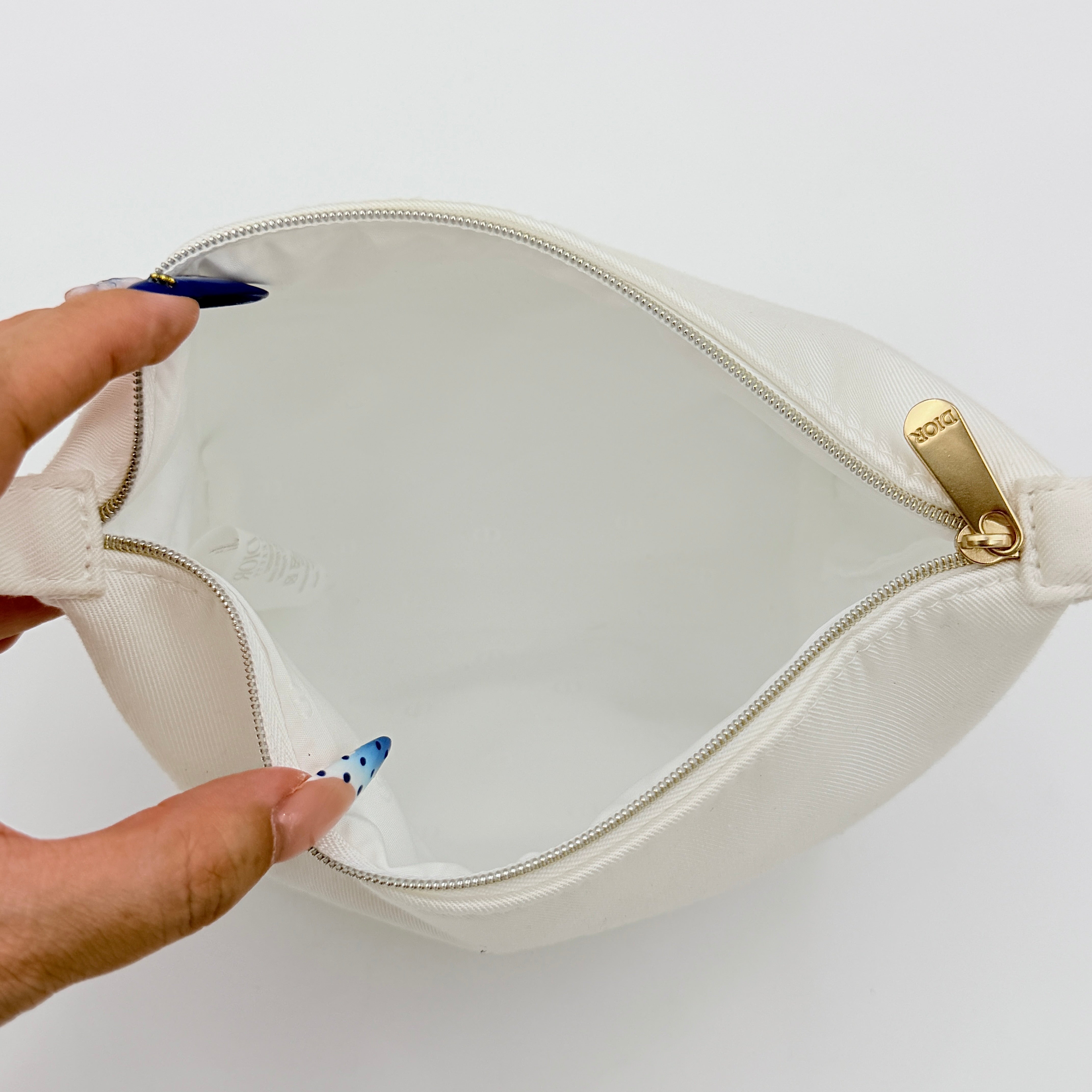 A structured white Dior pouch in twill with tonal logo embroidery and gold-tone zip, displayed against a pristine backdrop.