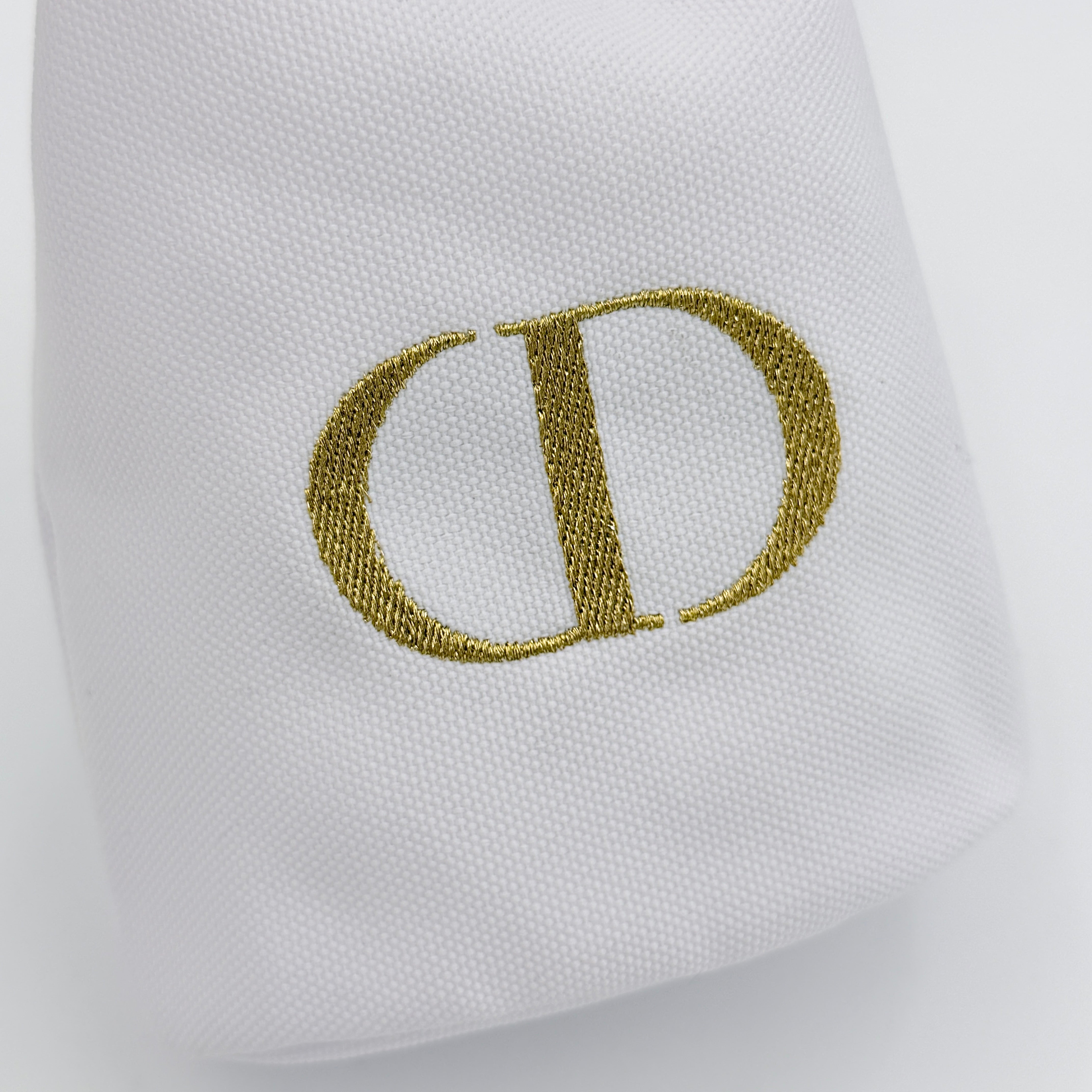 A structured white Dior drawstring pouch featuring a gold embroidered CD logo and white rope closure with gold-tone eyelets.