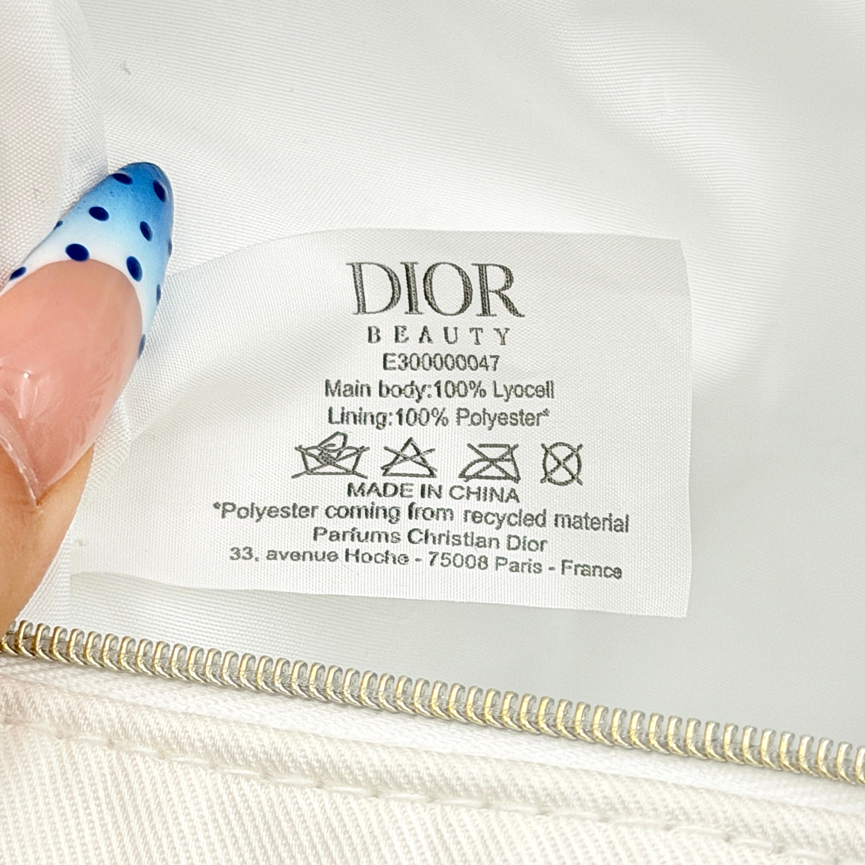 A structured white Dior pouch in twill with tonal logo embroidery and gold-tone zip, displayed against a pristine backdrop.