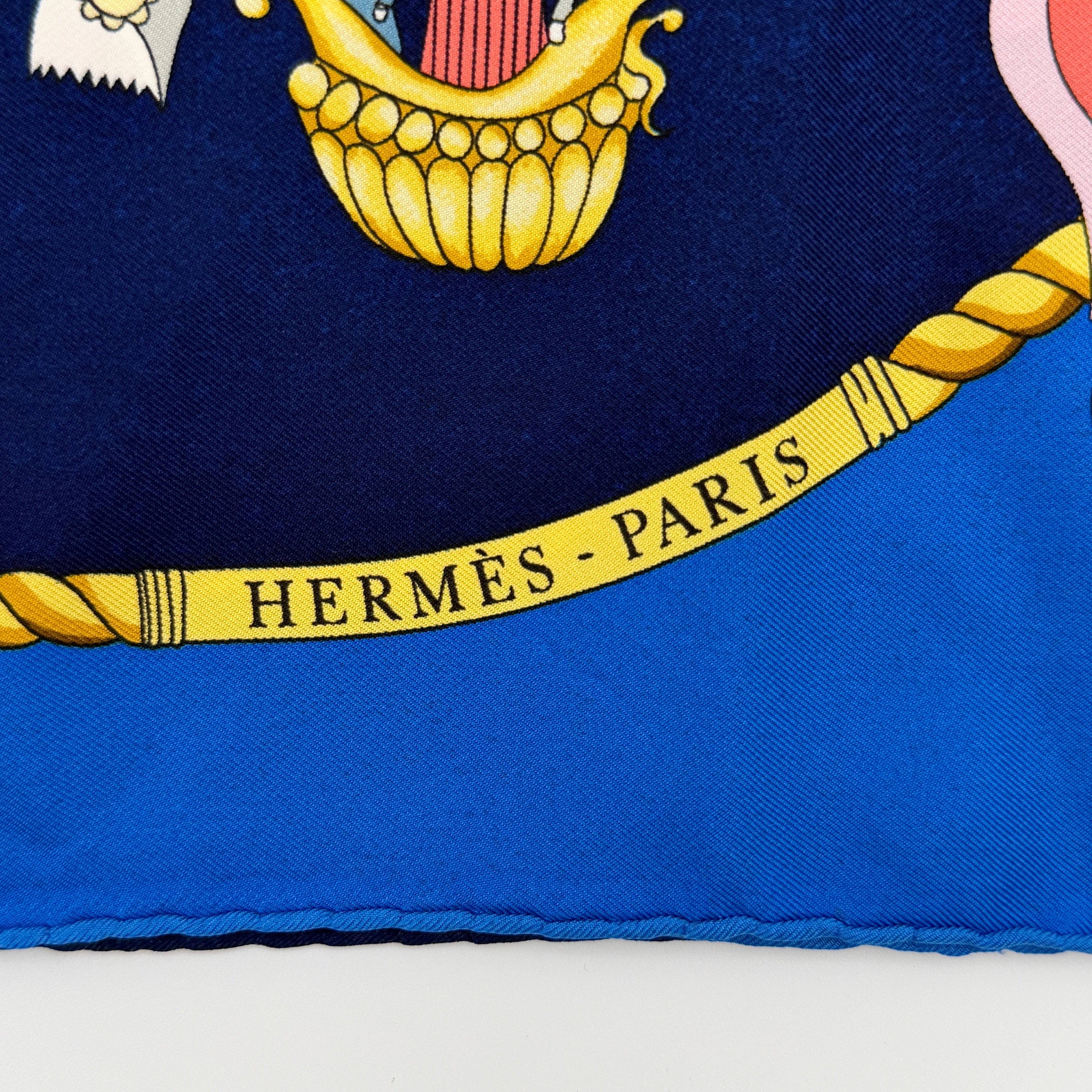 Hermès Les Folies du Ciel silk scarf in vivid multicolours with whimsical hot air balloons and golden rope border on a blue background.