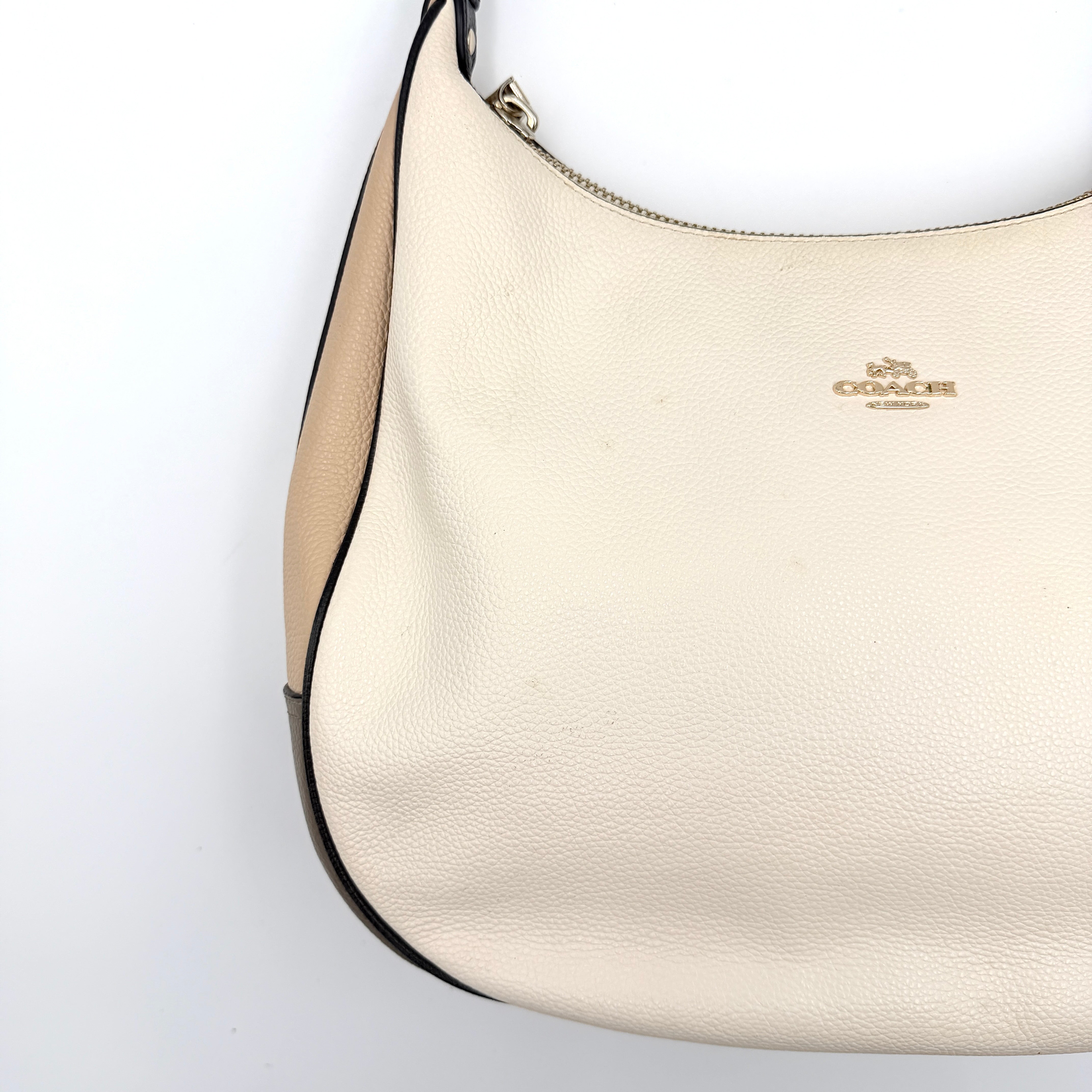 Coach Harley East West Hobo in cream and beige pebbled leather with a sculpted silhouette, black piping, and silver hardware.