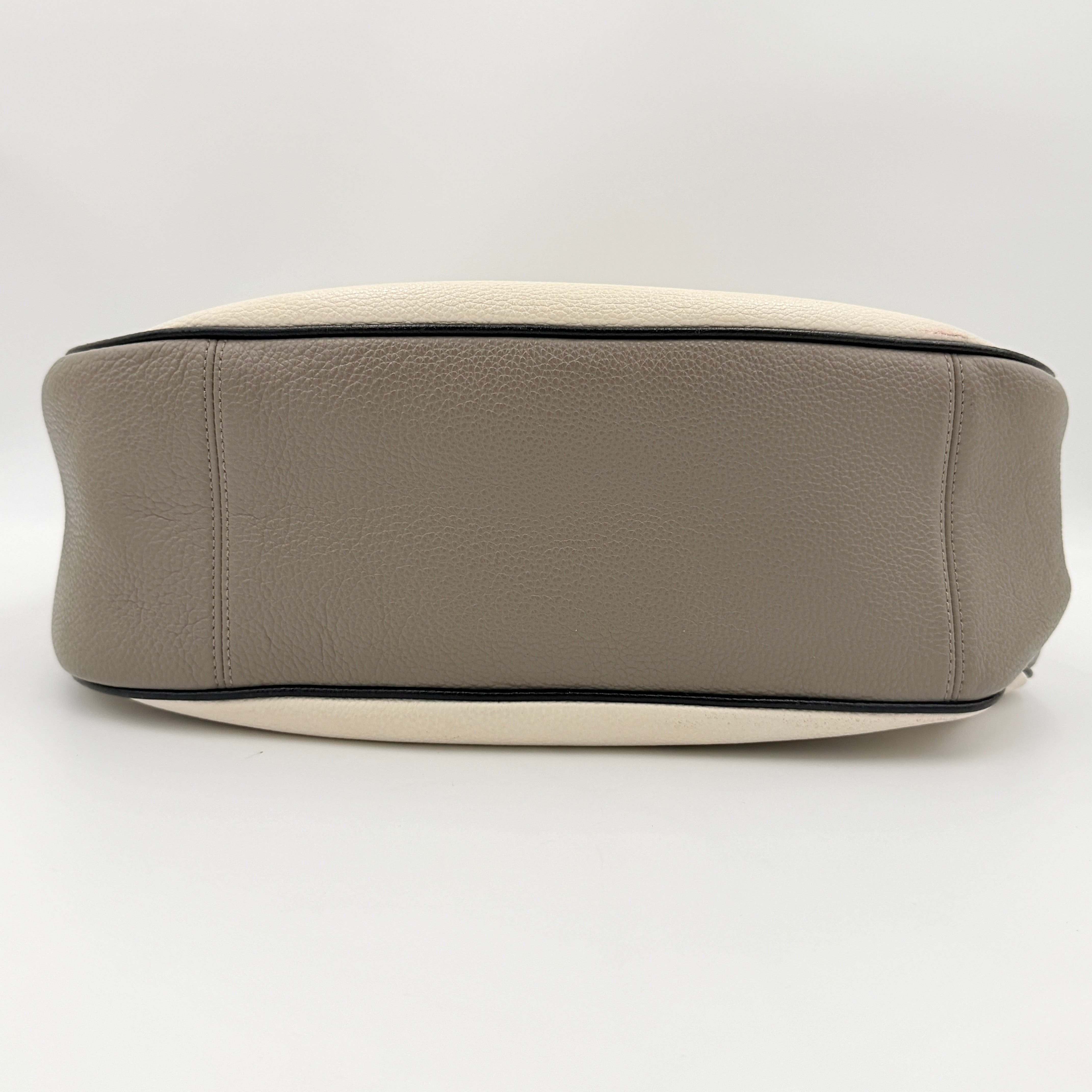 Coach Harley East West Hobo in cream and beige pebbled leather with a sculpted silhouette, black piping, and silver hardware.