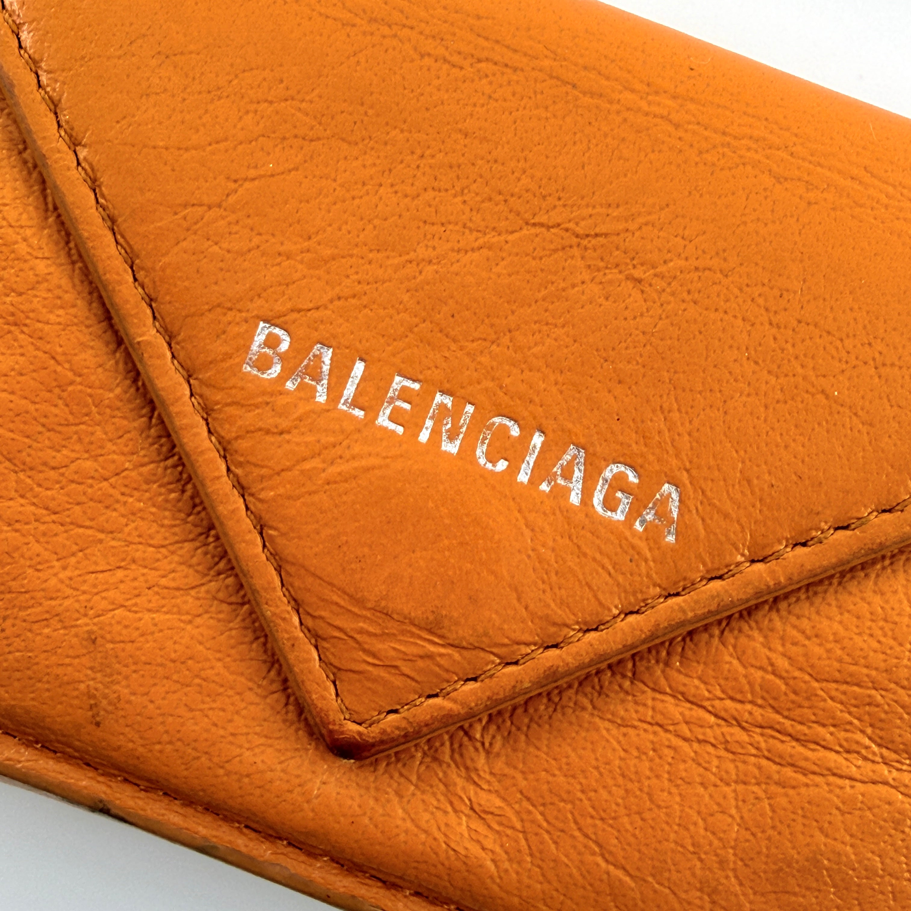 Balenciaga Papier Mini Wallet in vibrant orange grained leather, showcasing its envelope-style flap and silver logo detail.