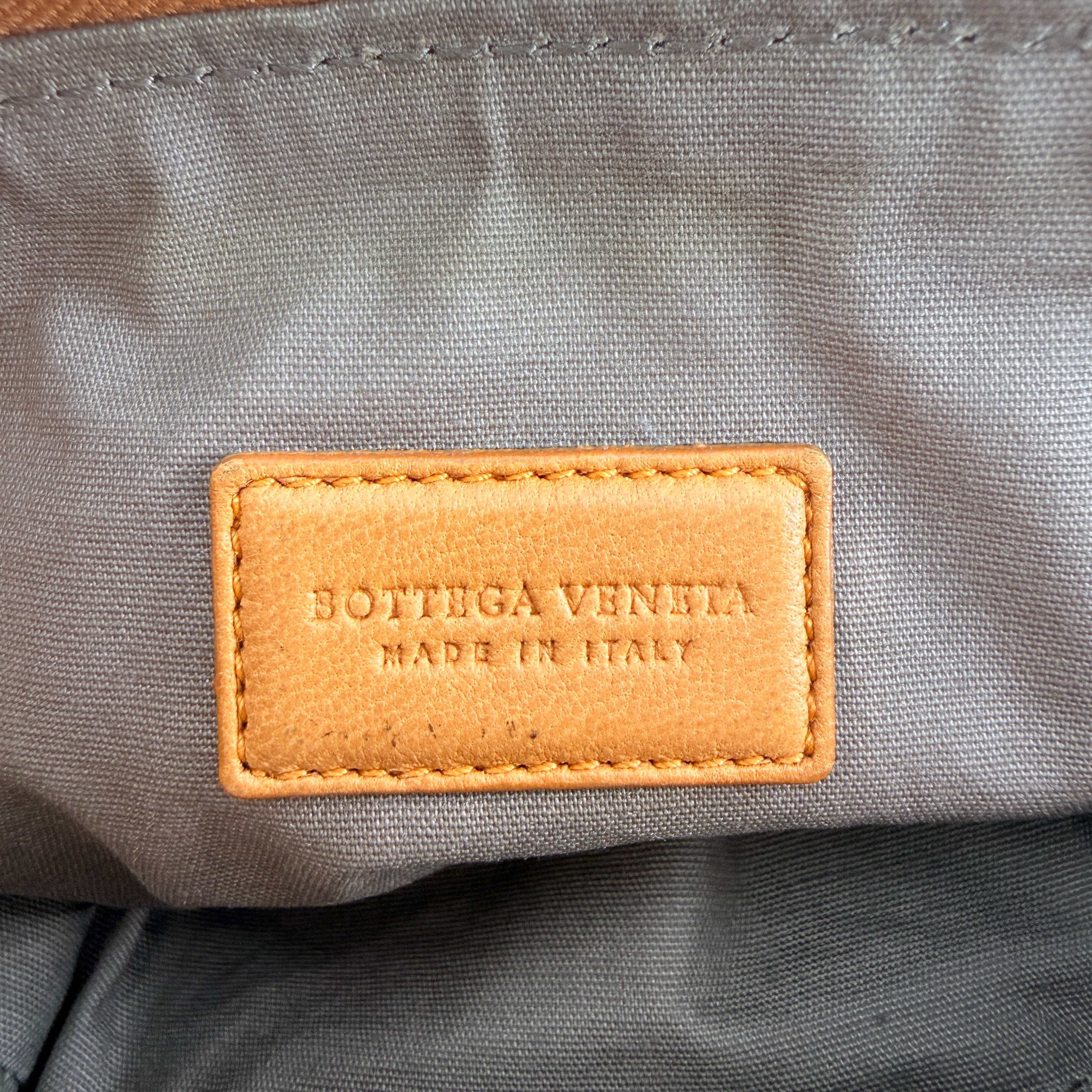 A Bottega Veneta brown Intrecciato leather pouch with gold zip and woven texture, displayed against a clean, minimal background.