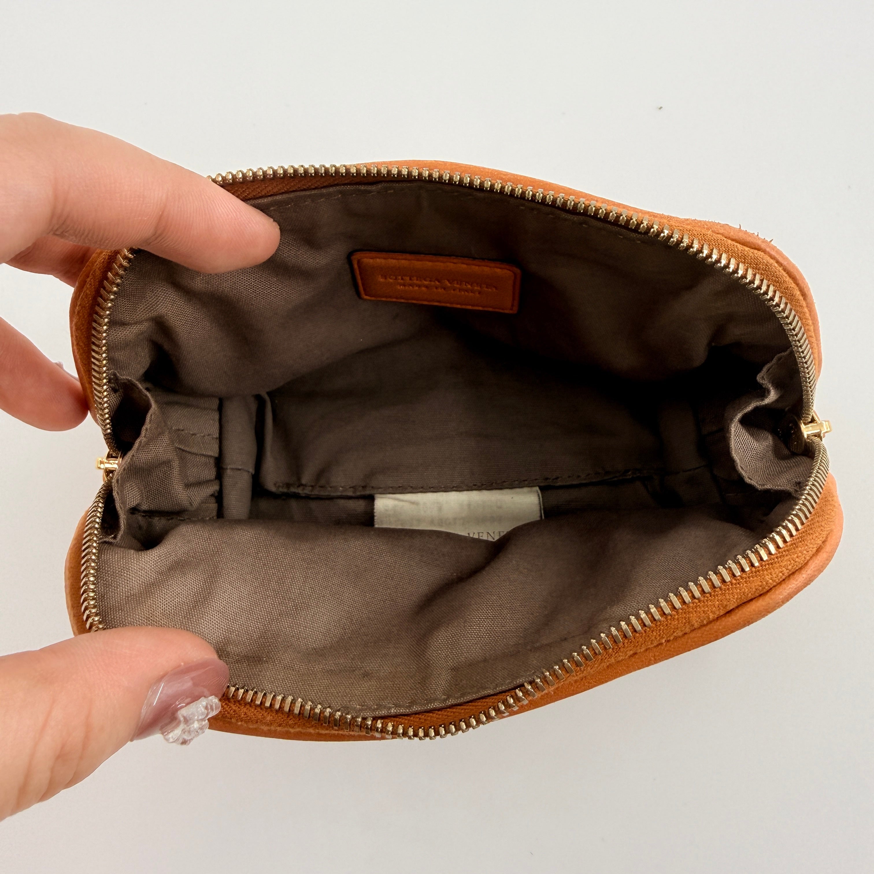 A Bottega Veneta brown Intrecciato leather pouch with gold zip and woven texture, displayed against a clean, minimal background.