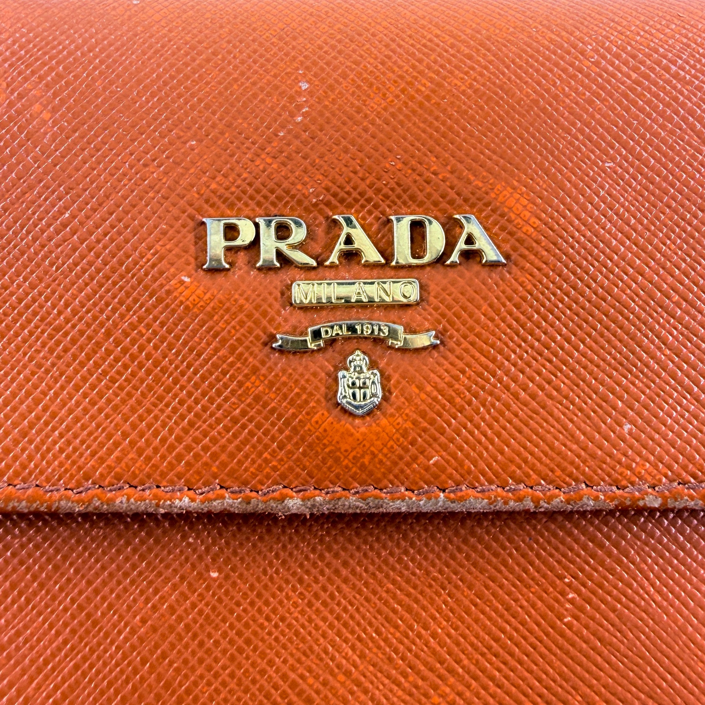 Prada Saffiano Leather Trifold Wallet in brown leather with gold-tone logo, showcasing its structured flap and crosshatch texture.