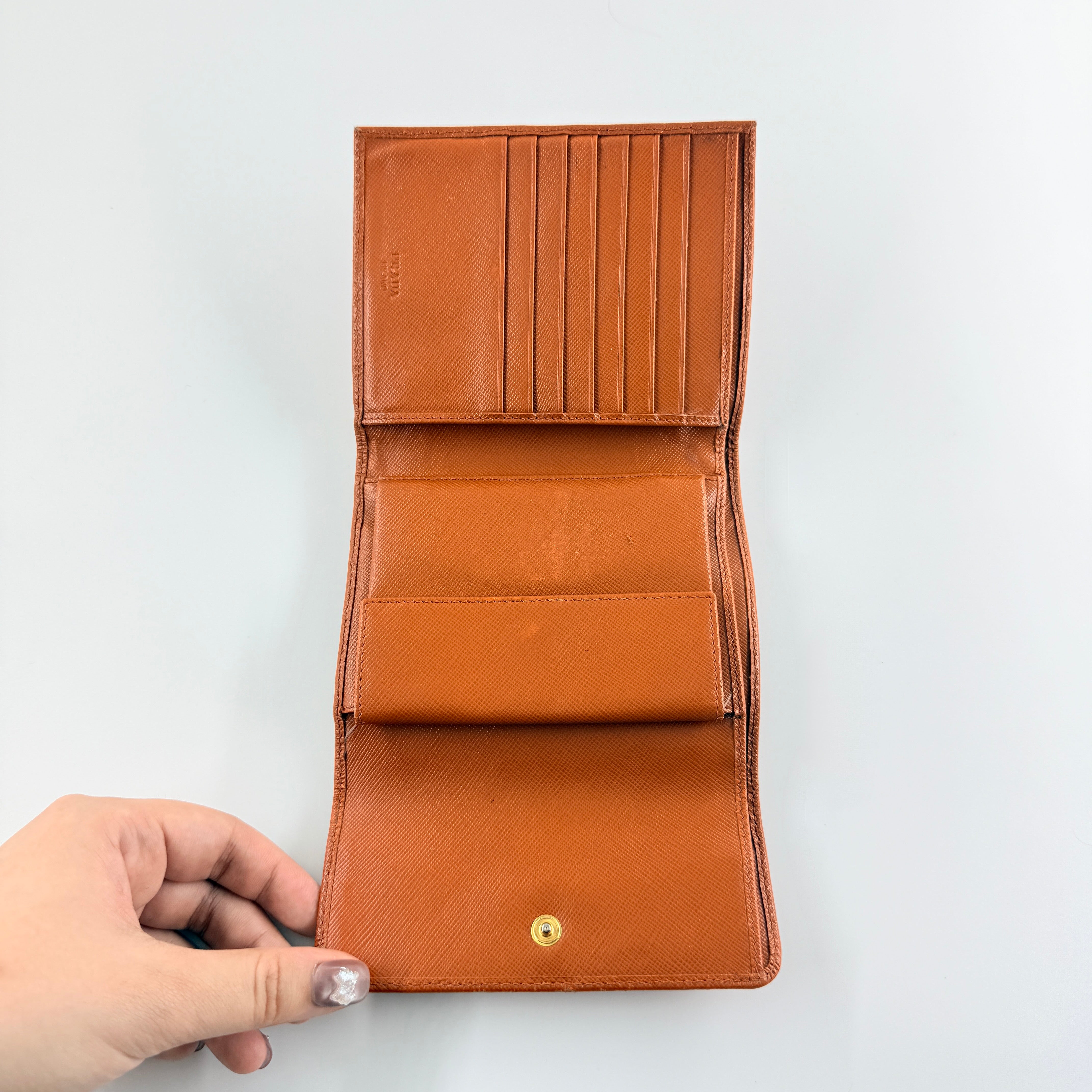 Prada Saffiano Leather Trifold Wallet in brown leather with gold-tone logo, showcasing its structured flap and crosshatch texture.