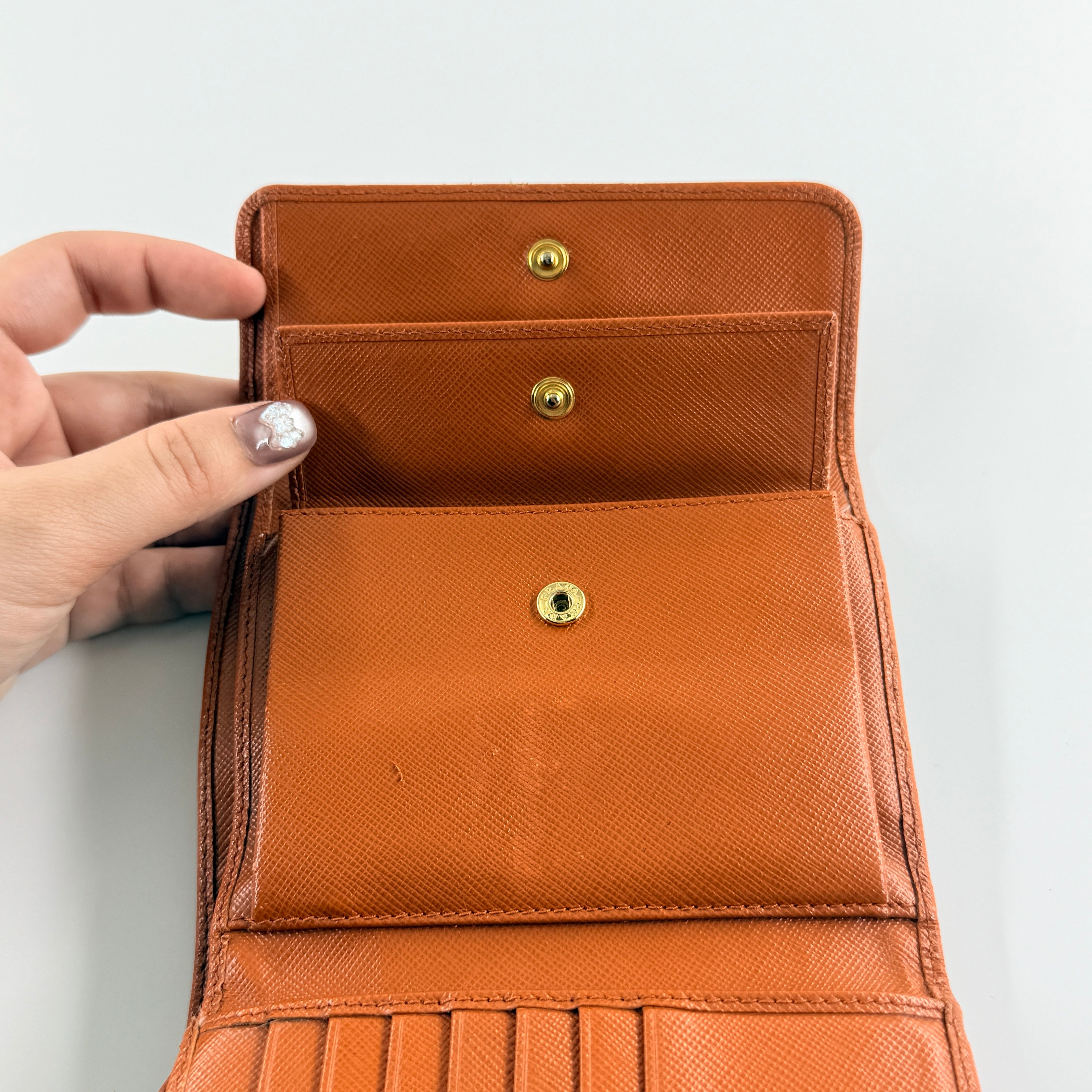 Prada Saffiano Leather Trifold Wallet in brown leather with gold-tone logo, showcasing its structured flap and crosshatch texture.