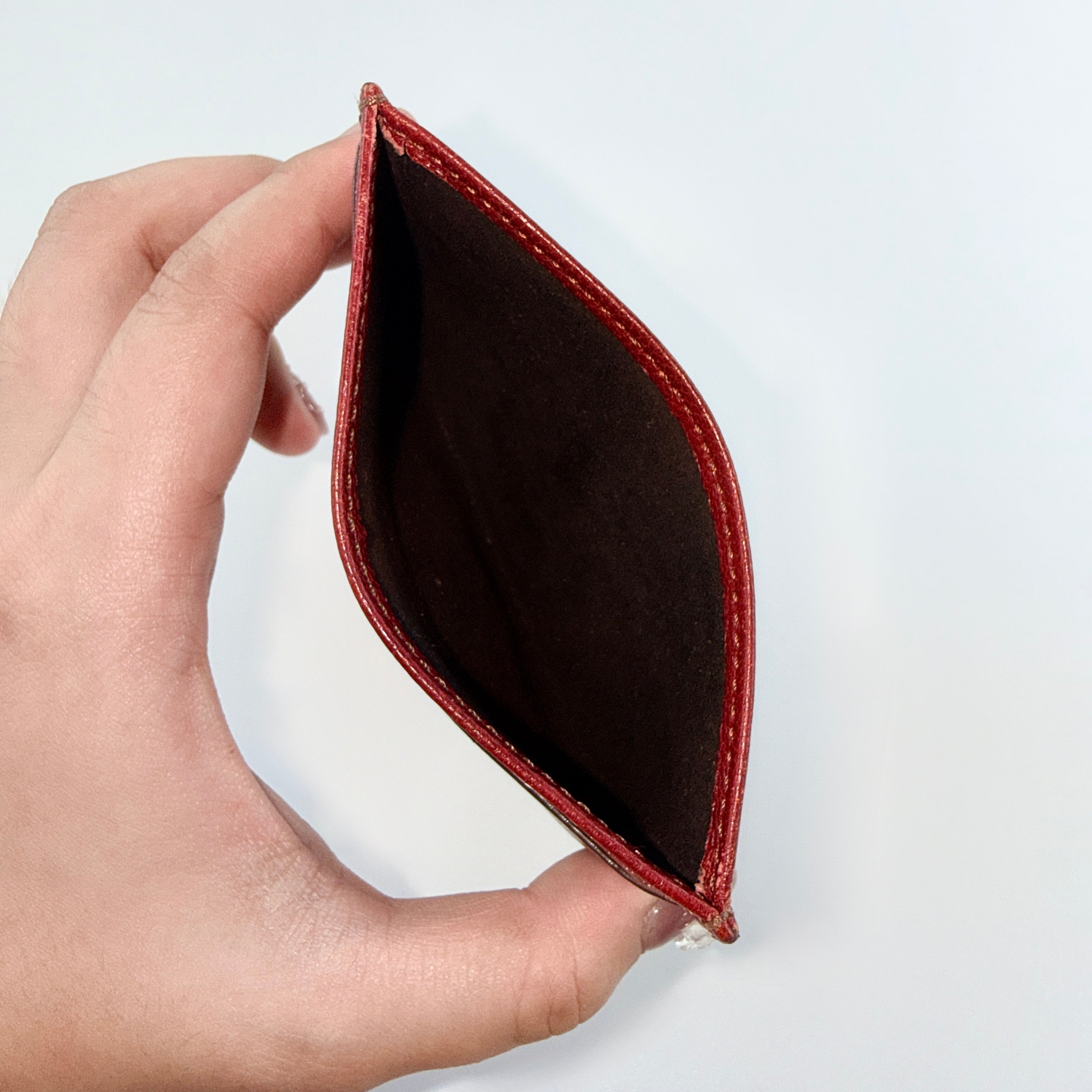 Must de Cartier burgundy leather cardholder with visible natural texture and Cartier script logo, photographed against a clean background.