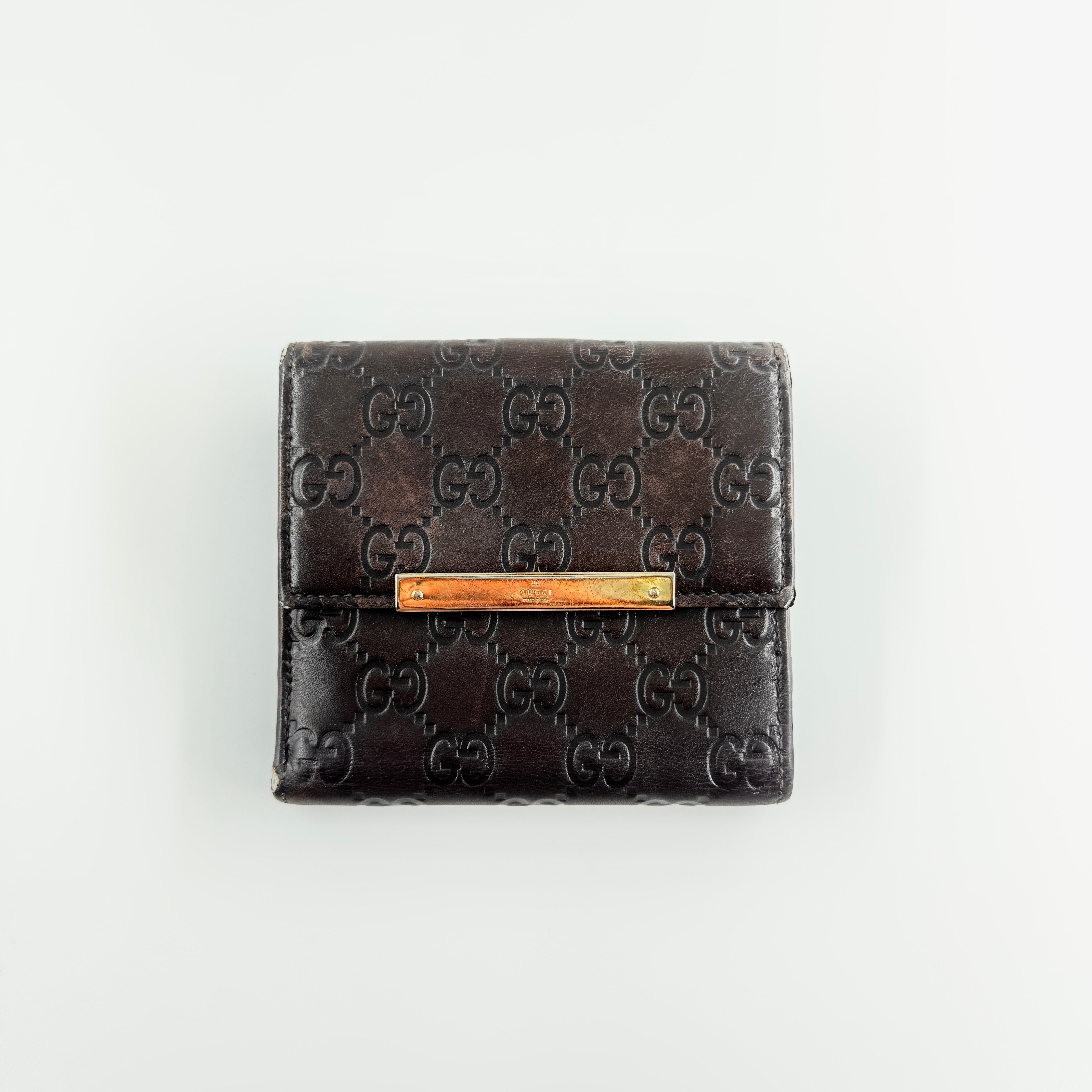 Front-facing Gucci GG Monogram Guccissima wallet in deep brown embossed leather with gold-tone bar accent.