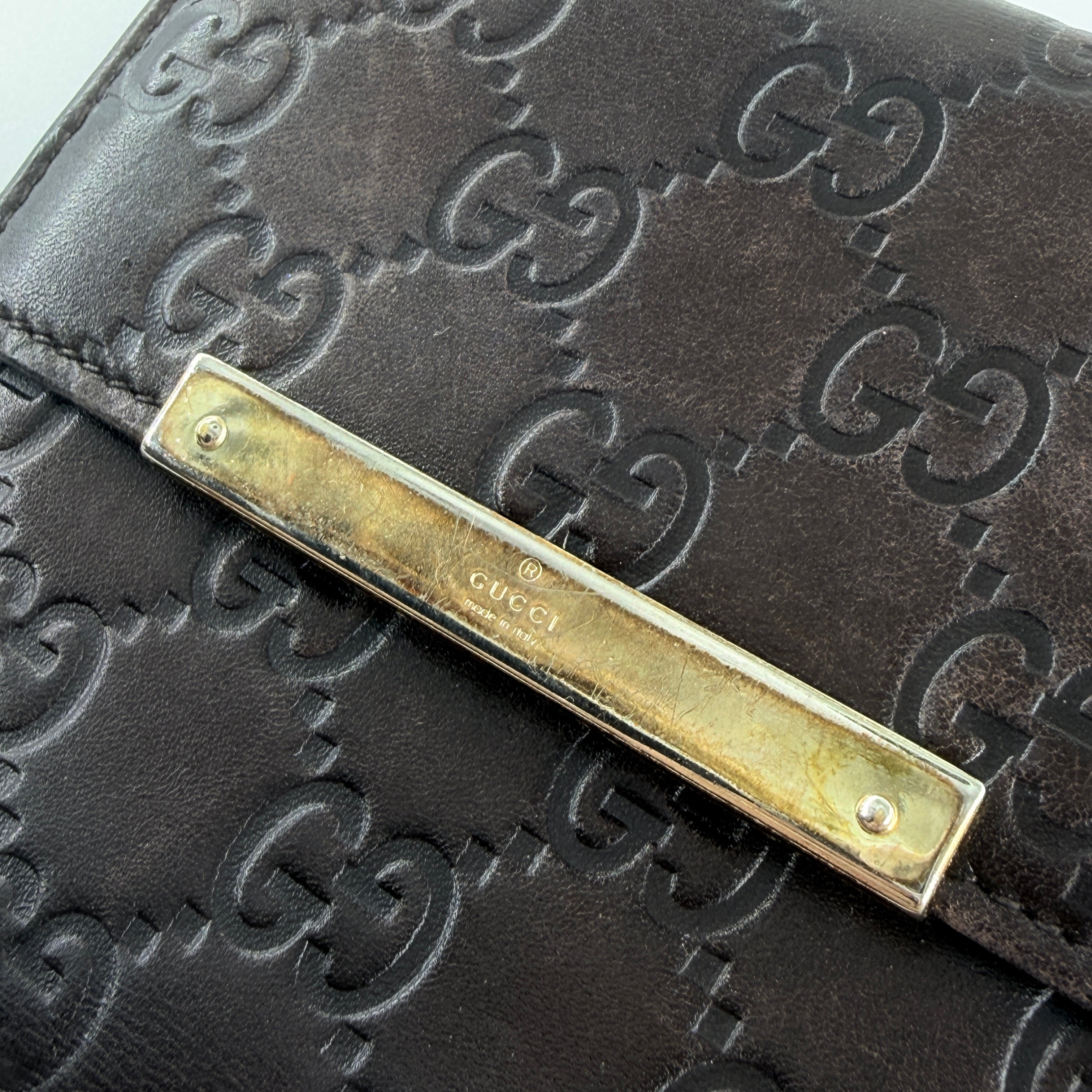 Front-facing Gucci GG Monogram Guccissima wallet in deep brown embossed leather with gold-tone bar accent.