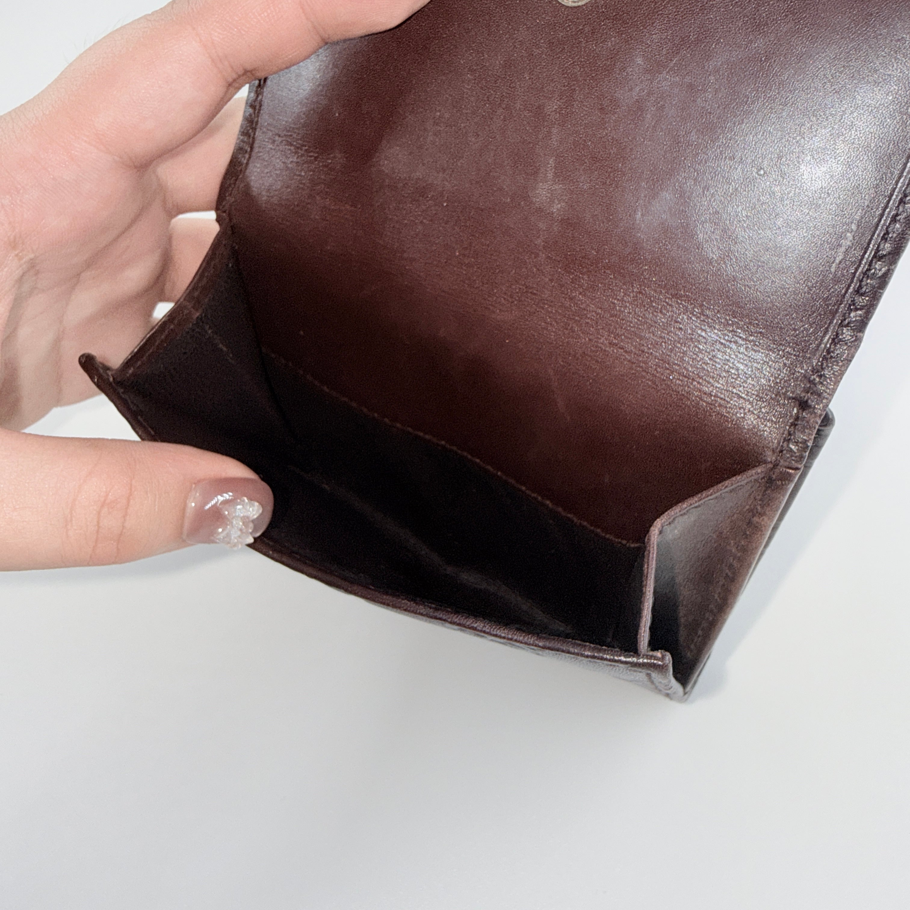 Front-facing Gucci GG Monogram Guccissima wallet in deep brown embossed leather with gold-tone bar accent.