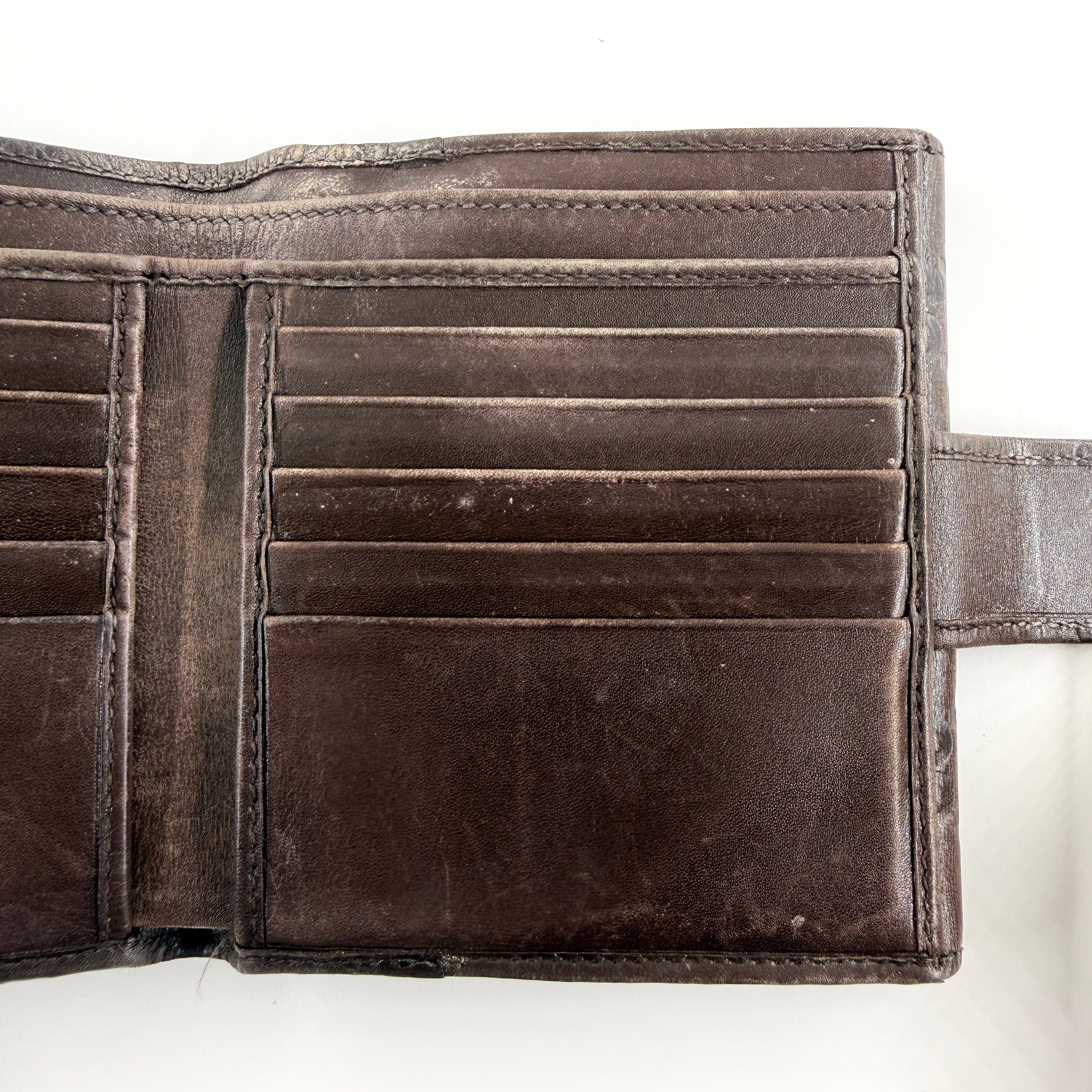 Front-facing Gucci GG Monogram Guccissima wallet in deep brown embossed leather with gold-tone bar accent.
