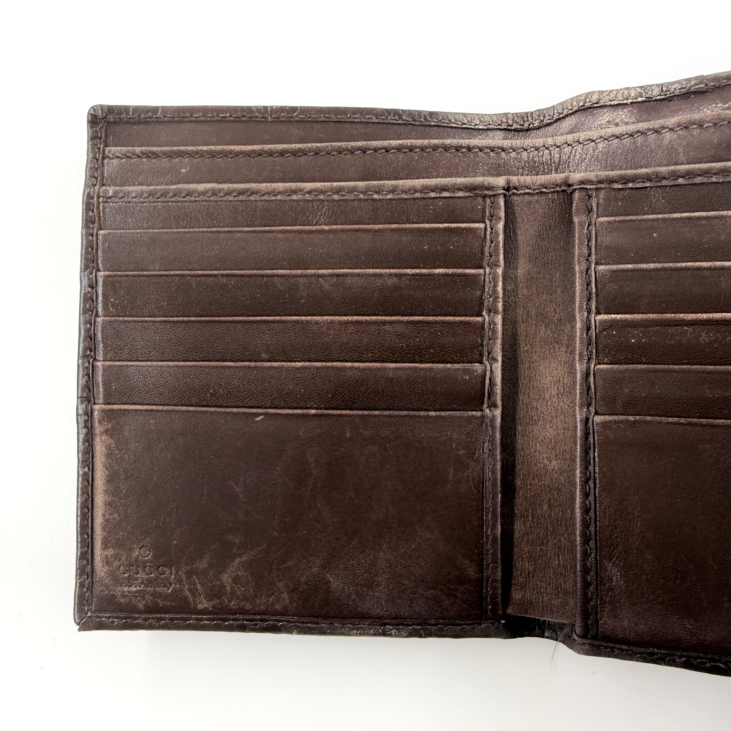Front-facing Gucci GG Monogram Guccissima wallet in deep brown embossed leather with gold-tone bar accent.