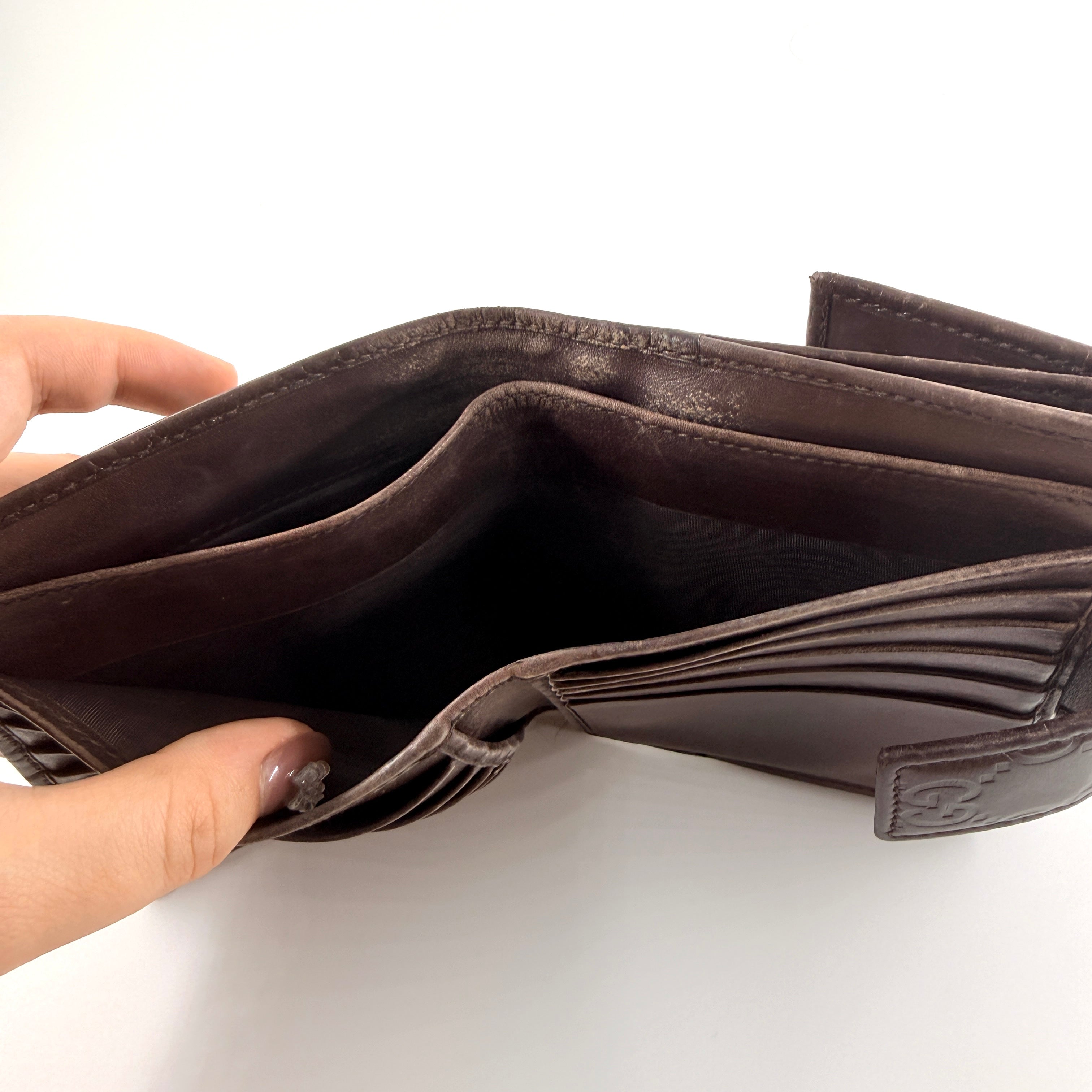 Front-facing Gucci GG Monogram Guccissima wallet in deep brown embossed leather with gold-tone bar accent.