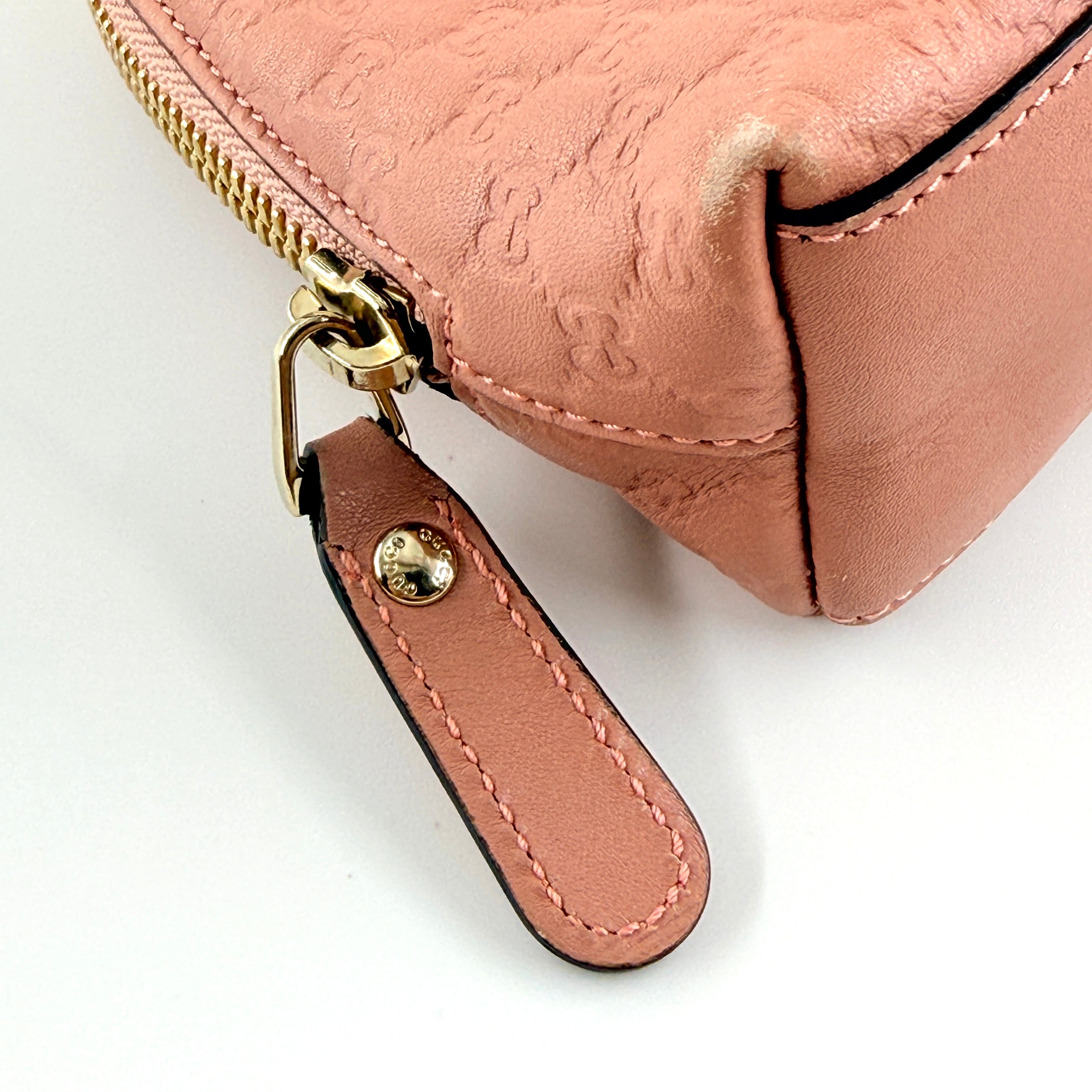 Gucci GG Monogram Guccissima cosmetic pouch in blush pink leather with signature embossed motif and gold-tone zip hardware.