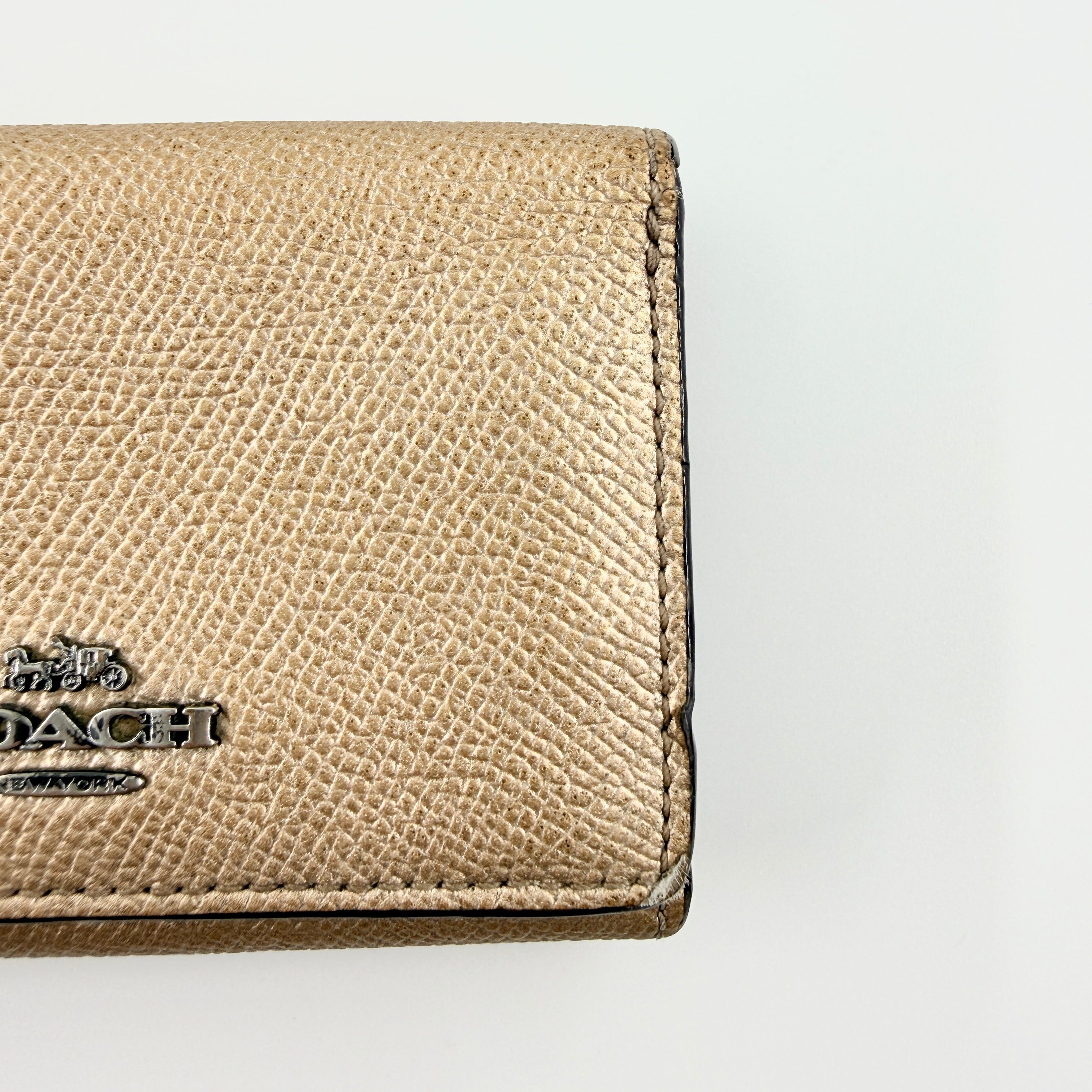 Coach metallic gold small flap wallet with silver logo plaque and crosshatch textured leather.