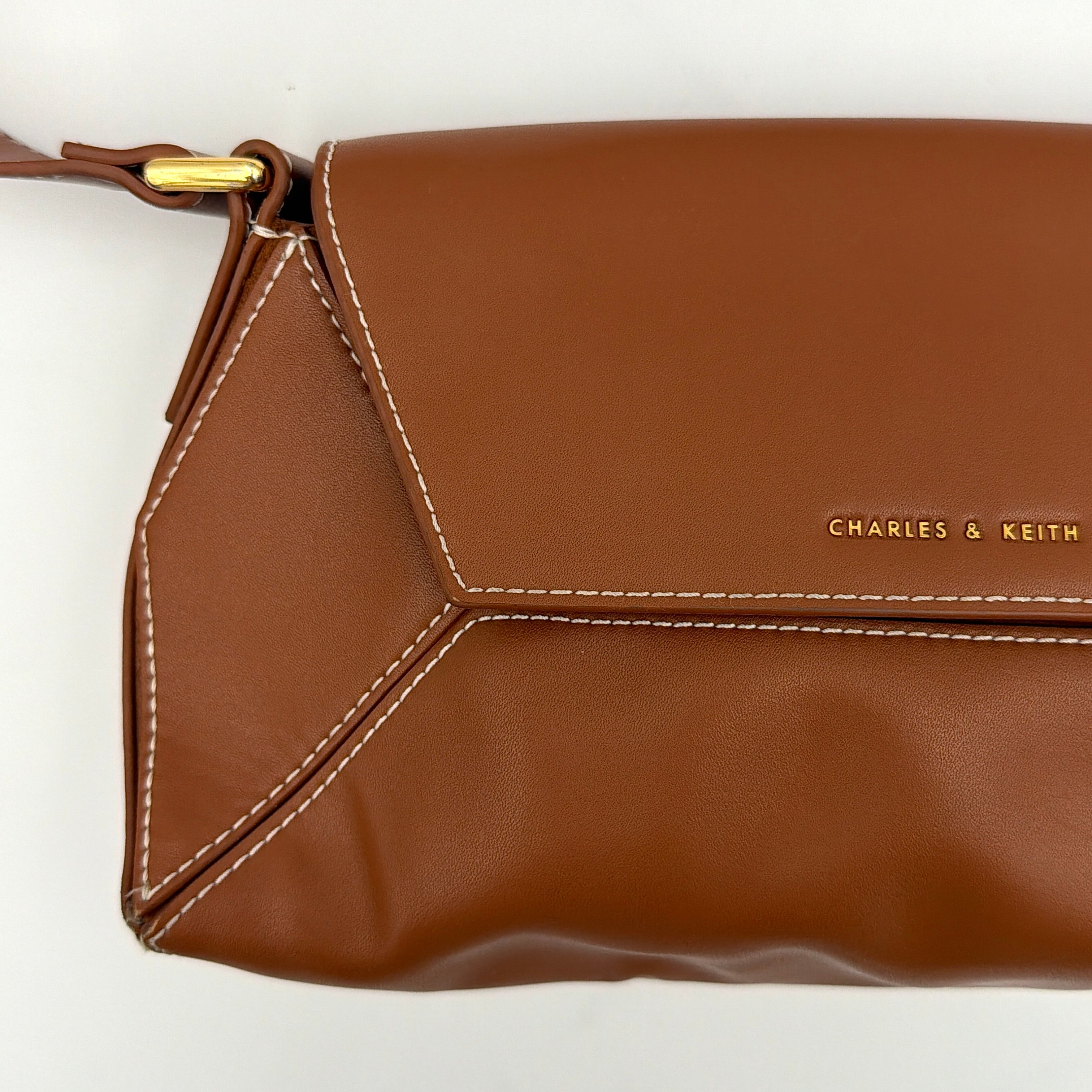 Charles & Keith Nasrin Geometric Crossbody Bag in brown faux leather with angular stitching, gold-tone hardware, and adjustable strap.