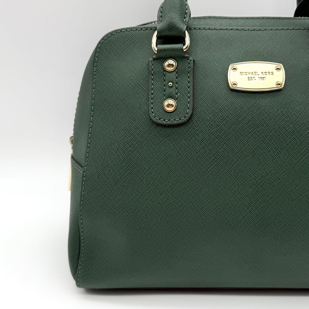 Michael Kors dark green Saffiano leather dome satchel with gold hardware and detachable strap, shown against a white background.