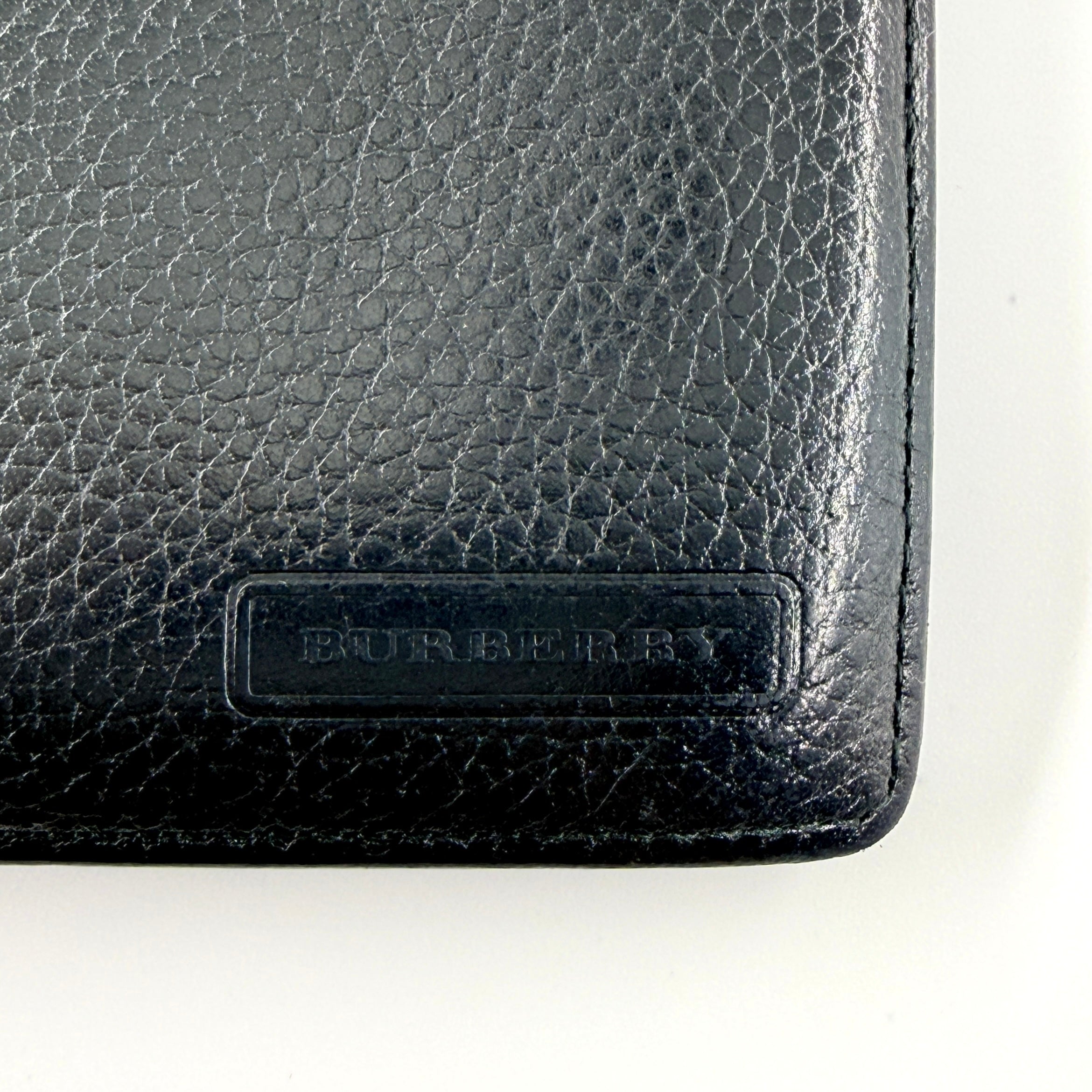 Burberry Nova Check bifold wallet in refined black grained leather with discreet embossed logo, presenting a minimal and polished silhouette.