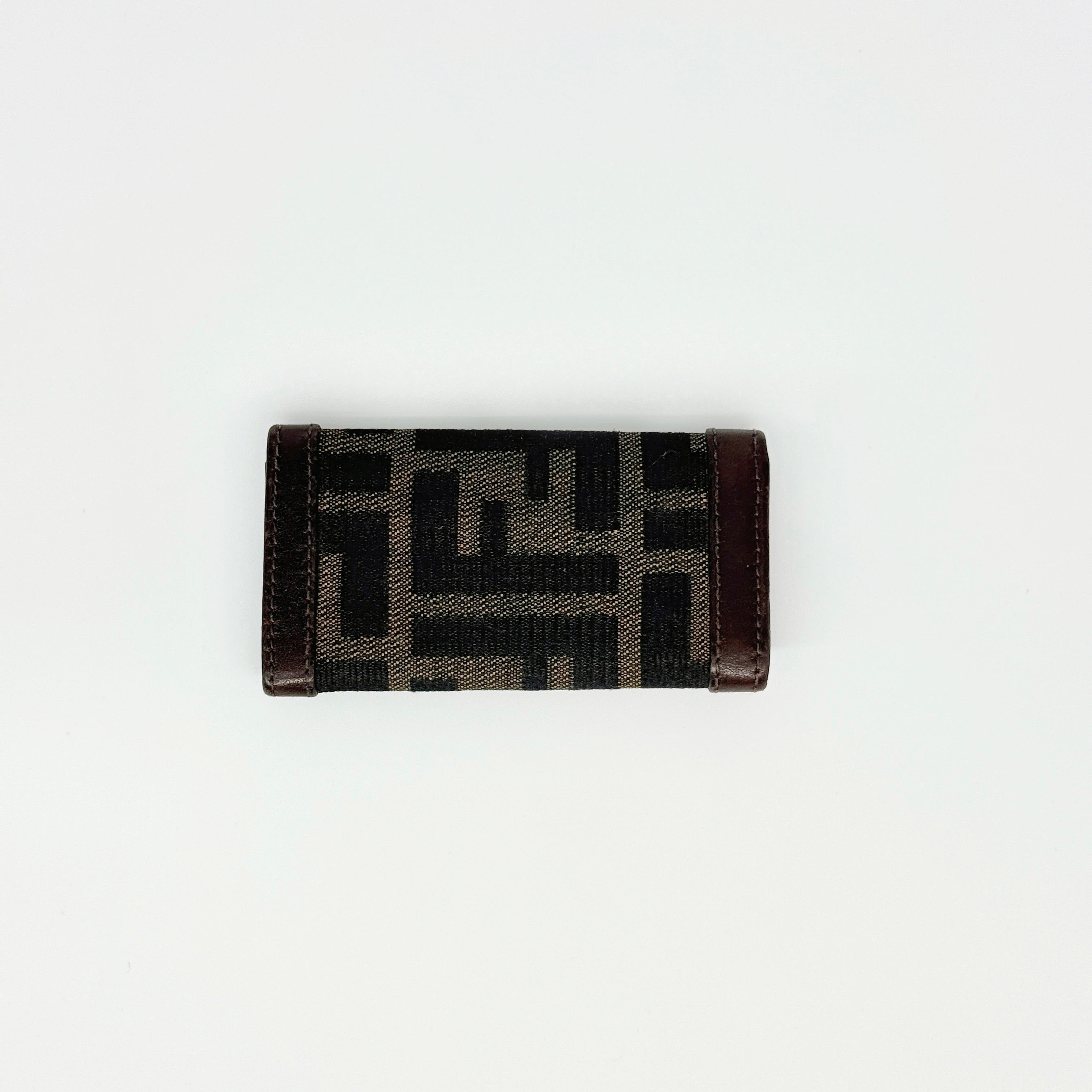 Fendi FF Zucca key case in brown canvas with dark brown leather trim and silver-tone hardware displayed closed against a white backdrop.