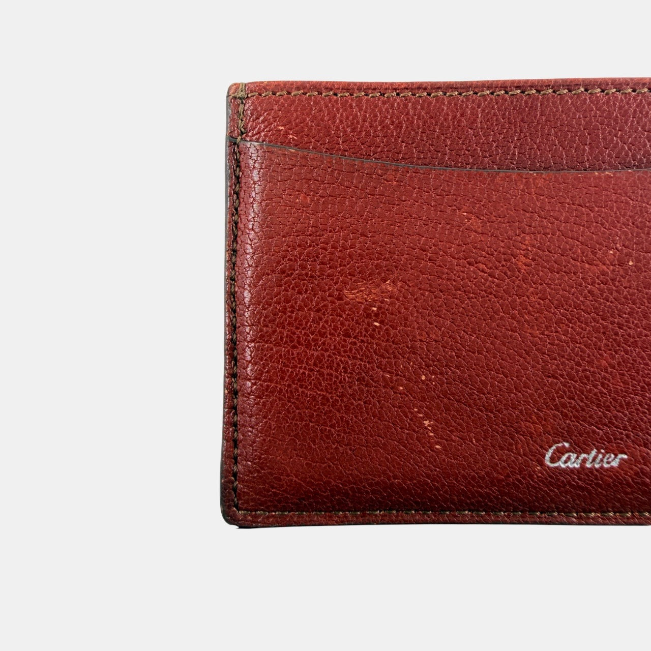 Must de Cartier burgundy leather cardholder with visible natural texture and Cartier script logo, photographed against a clean background.