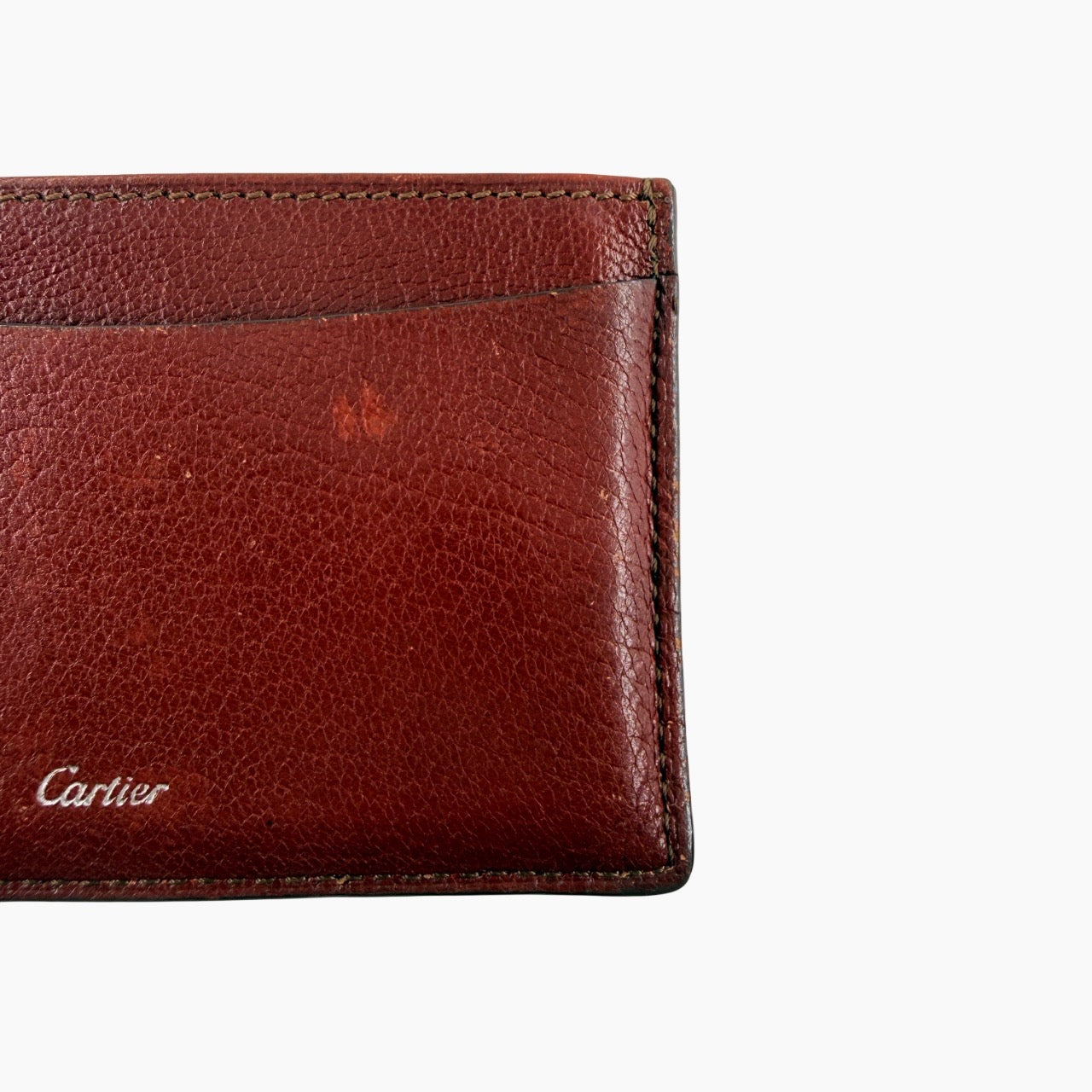 Must de Cartier burgundy leather cardholder with visible natural texture and Cartier script logo, photographed against a clean background.