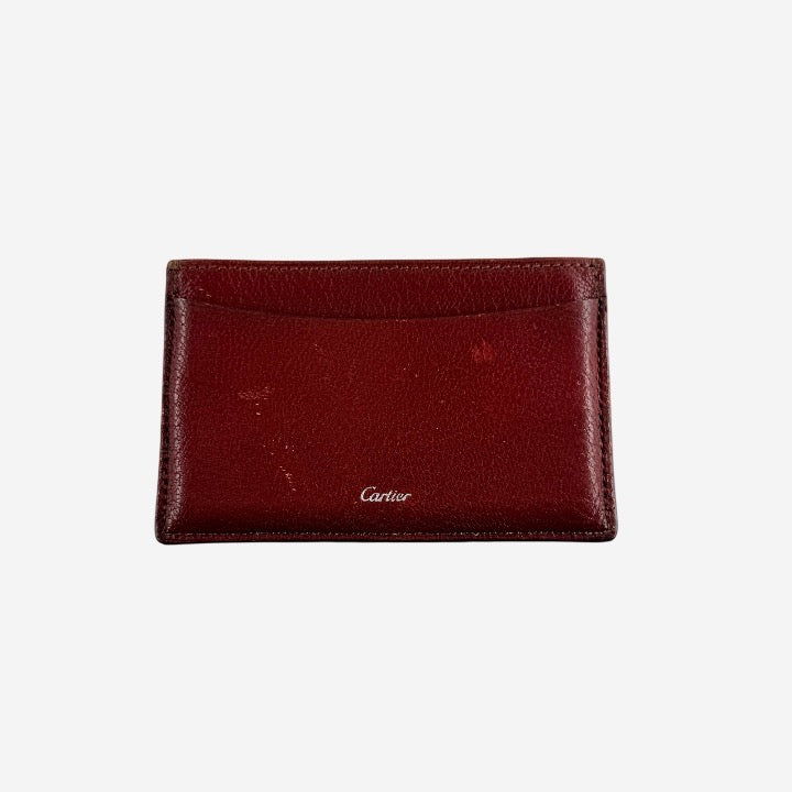 Must de Cartier burgundy leather cardholder with visible natural texture and Cartier script logo, photographed against a clean background.