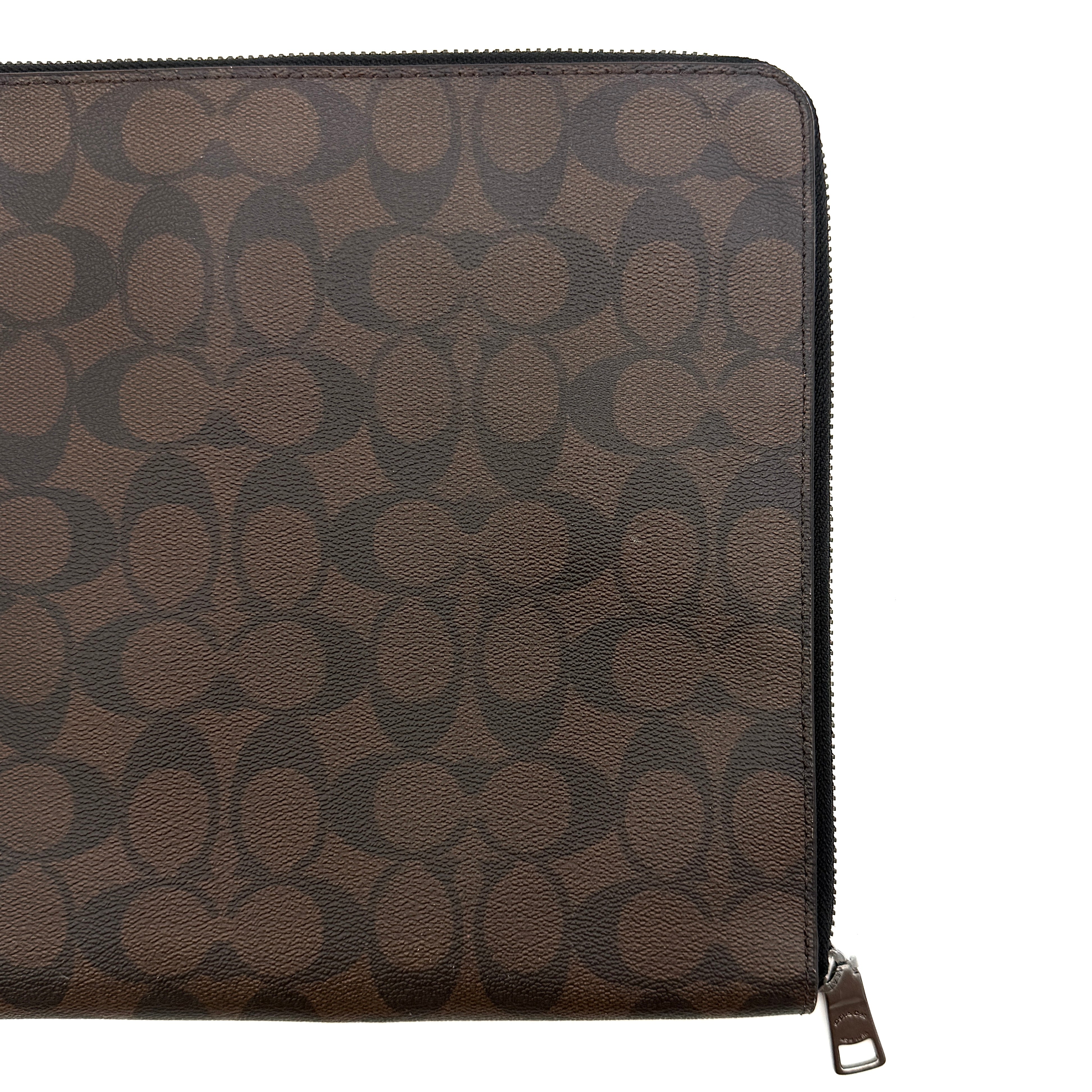 Coach Signature Zip Portfolio in brown and black monogram canvas with zip-around closure, displayed flat against a white background.
