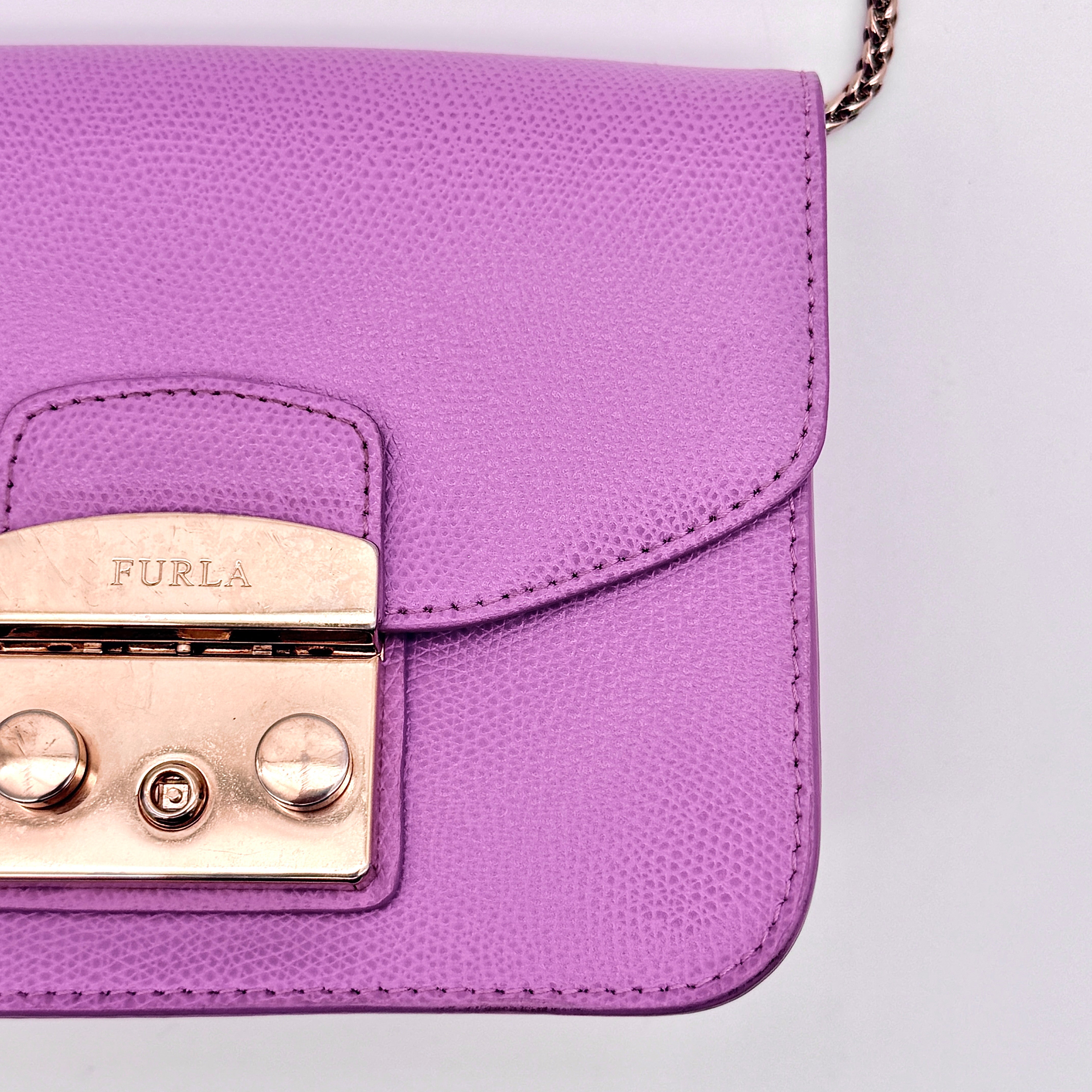 Furla Metropolis crossbody bag in pink grained leather with gold hardware and chain strap, displayed against a white background.
