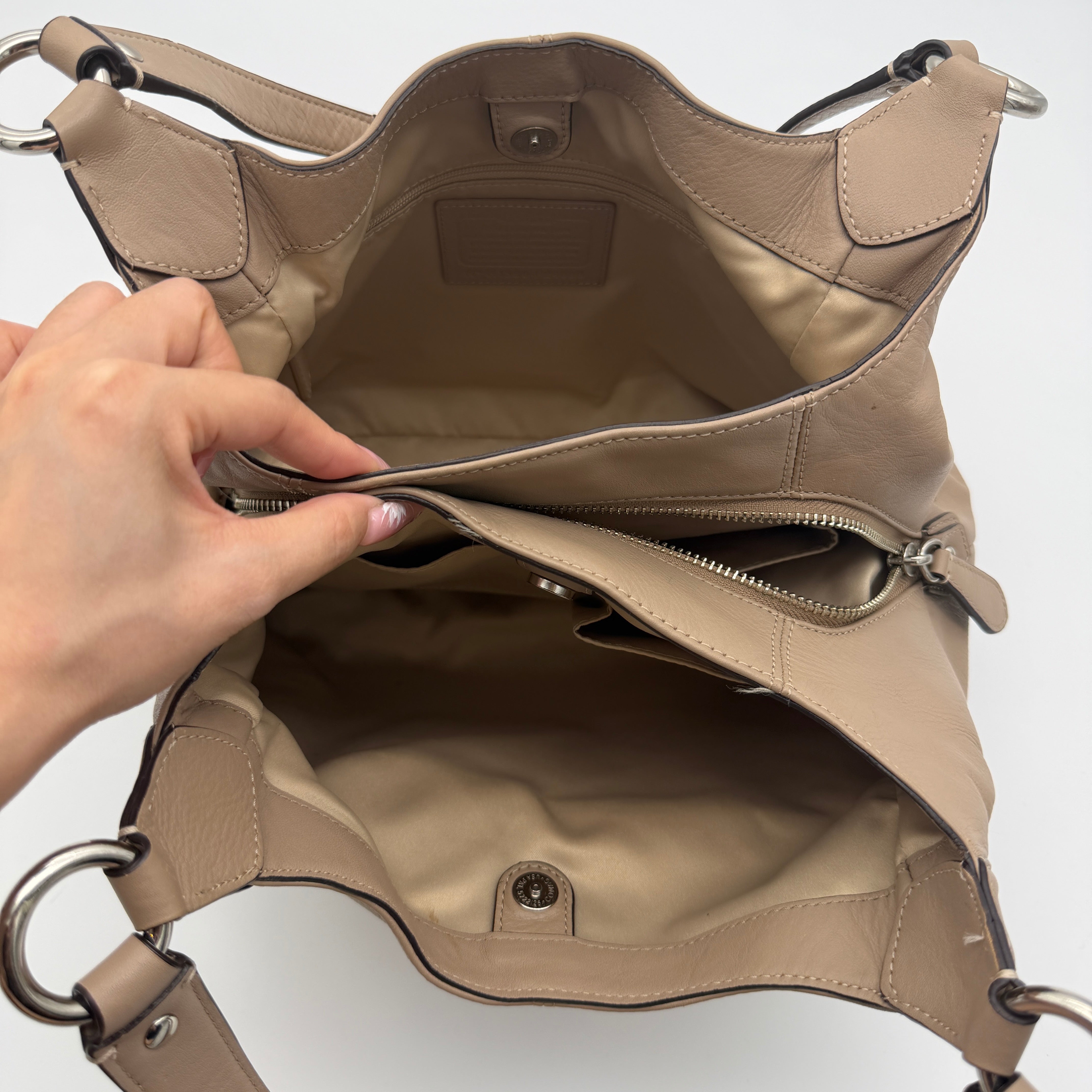 Coach Campbell Hobo shoulder bag in beige leather with silver hardware and front pocket, shown against a white background.