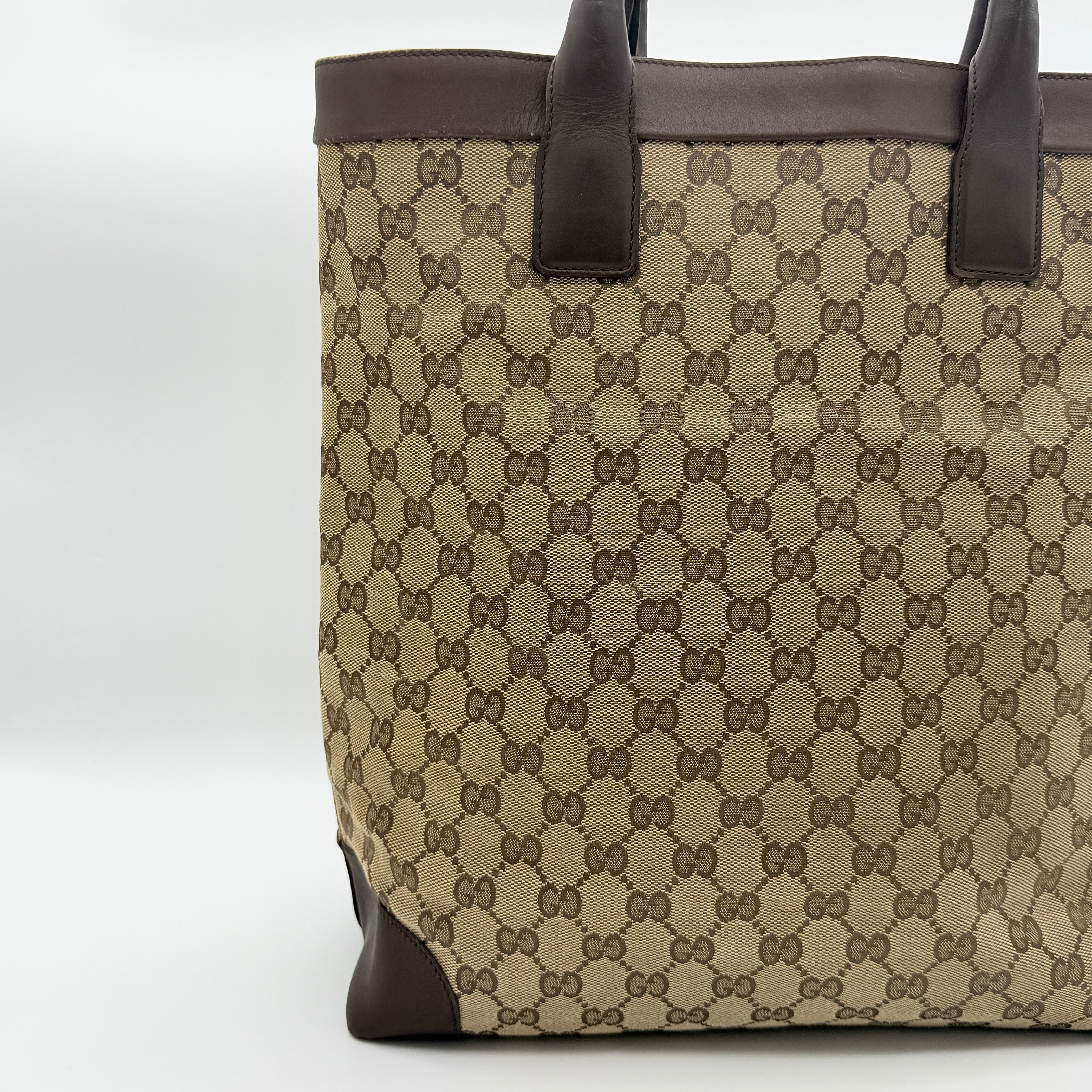 Front view of a Gucci GG Monogram Tote Bag in beige and brown canvas with dark leather trim and structured handles.